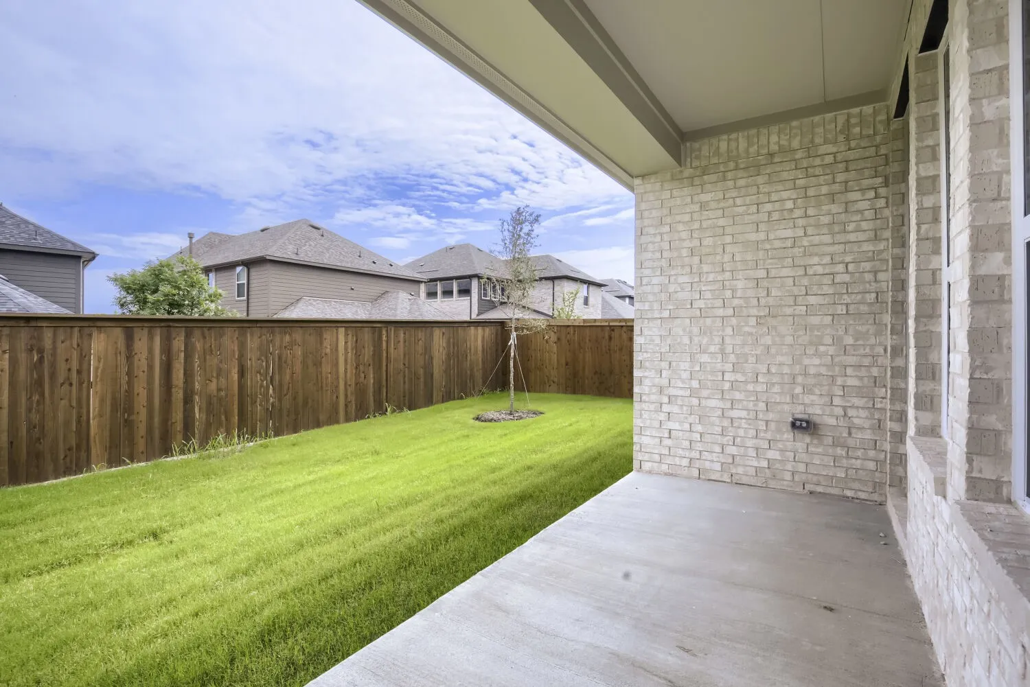 Covered outdoor patio with a concrete surface, light-colored brick exterior, and a spacious green lawn