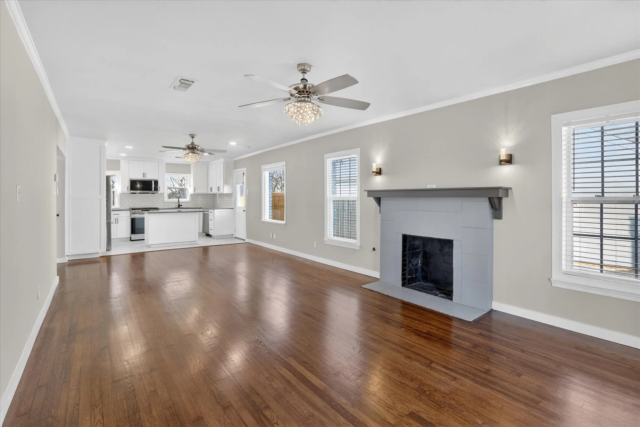 Spacious open living room with wood burning fireplace, beautiful wood floors, two ceiling fans, and lots of natural light.