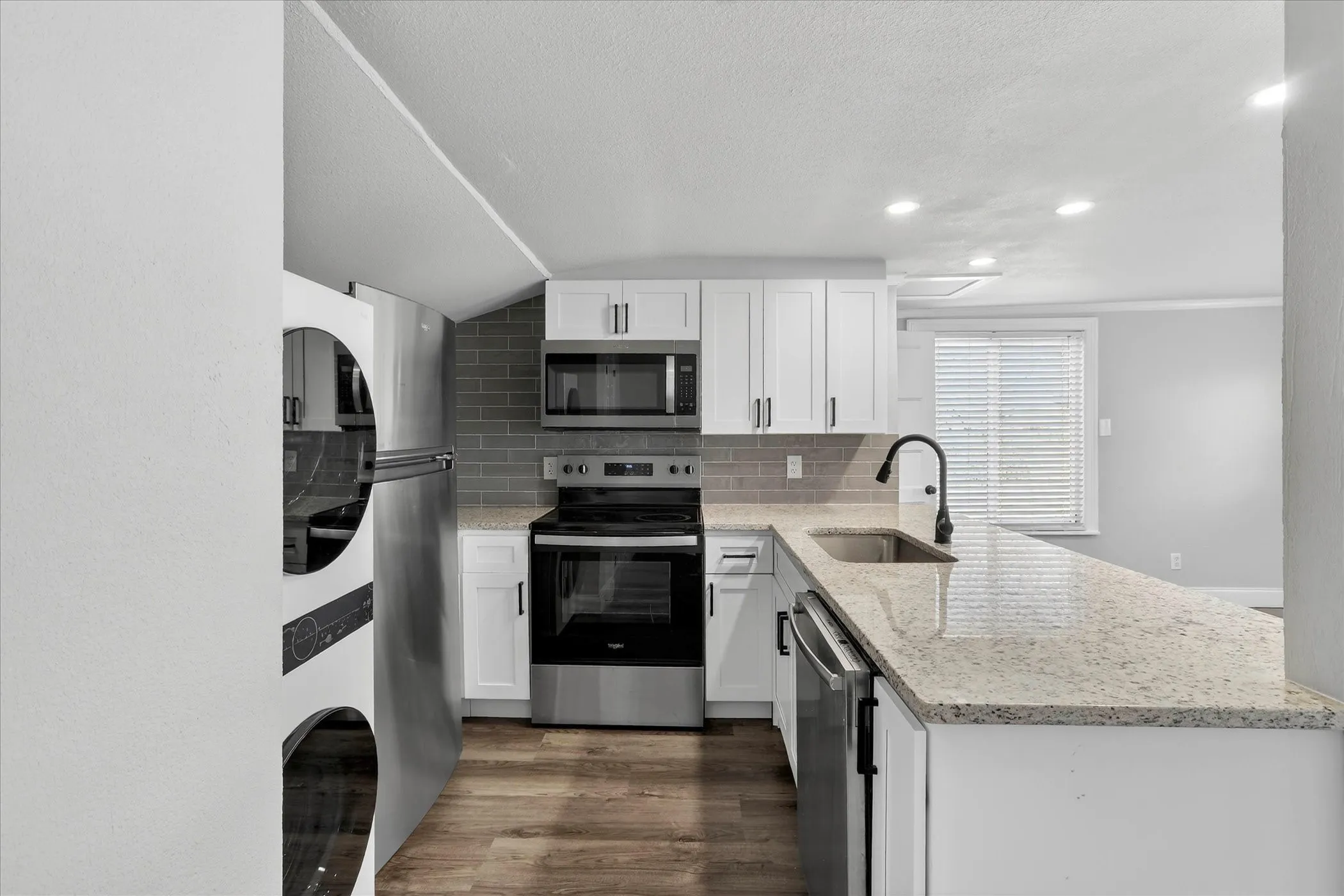 Kitchen in the guesthouse with white cabinetry, dishwasher, built in microwave, refrigerator, electric range, and washer and dryer.