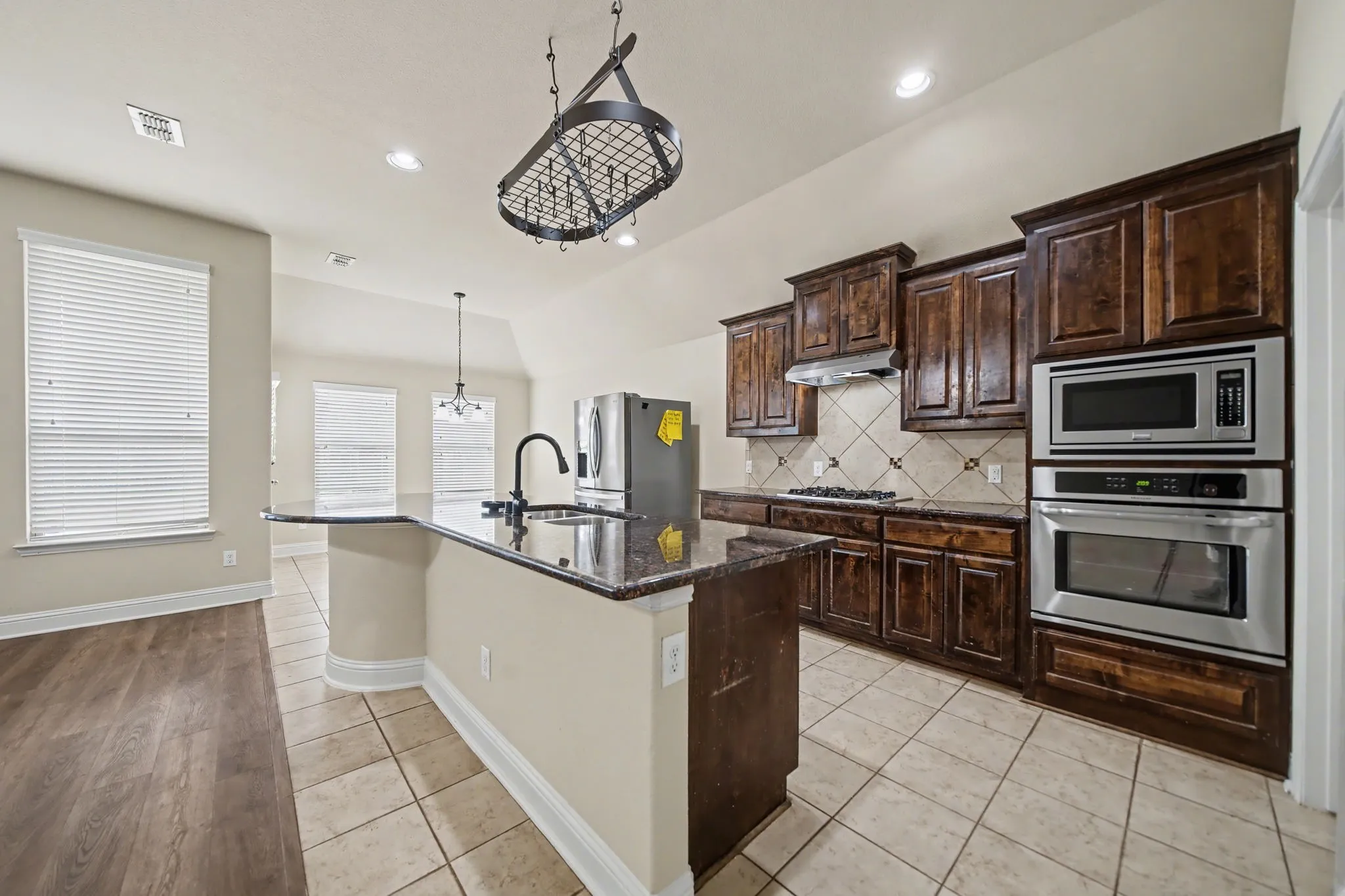 Kitchen with dark brown cabinetry, light tile patterned floors, stainless steel appliances, dark stone countertops, and tasteful backsplash