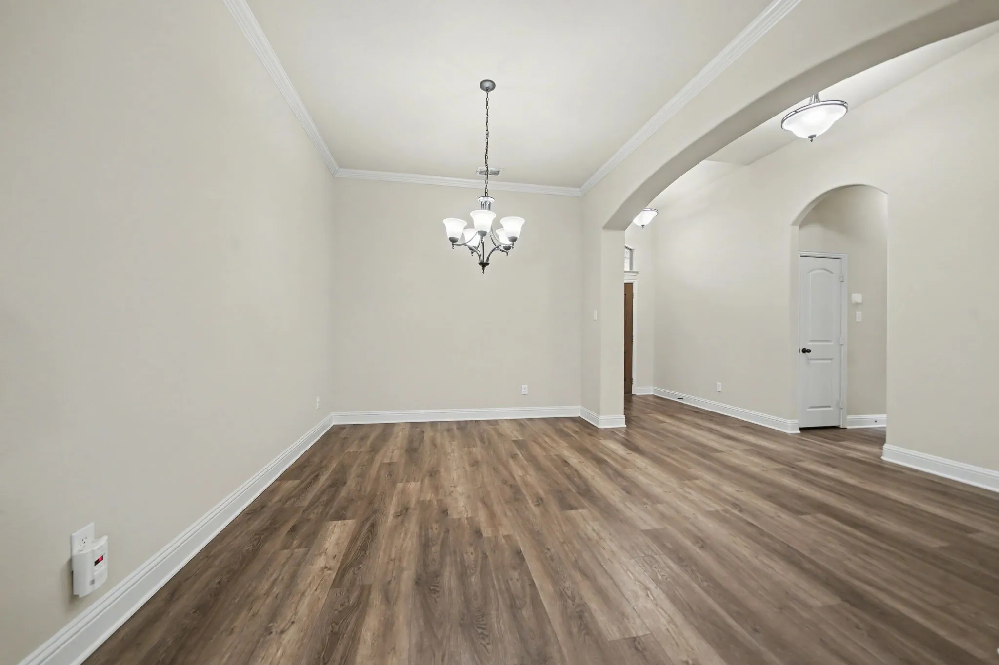 Unfurnished dining area with dark wood finished floors, a chandelier, and crown molding