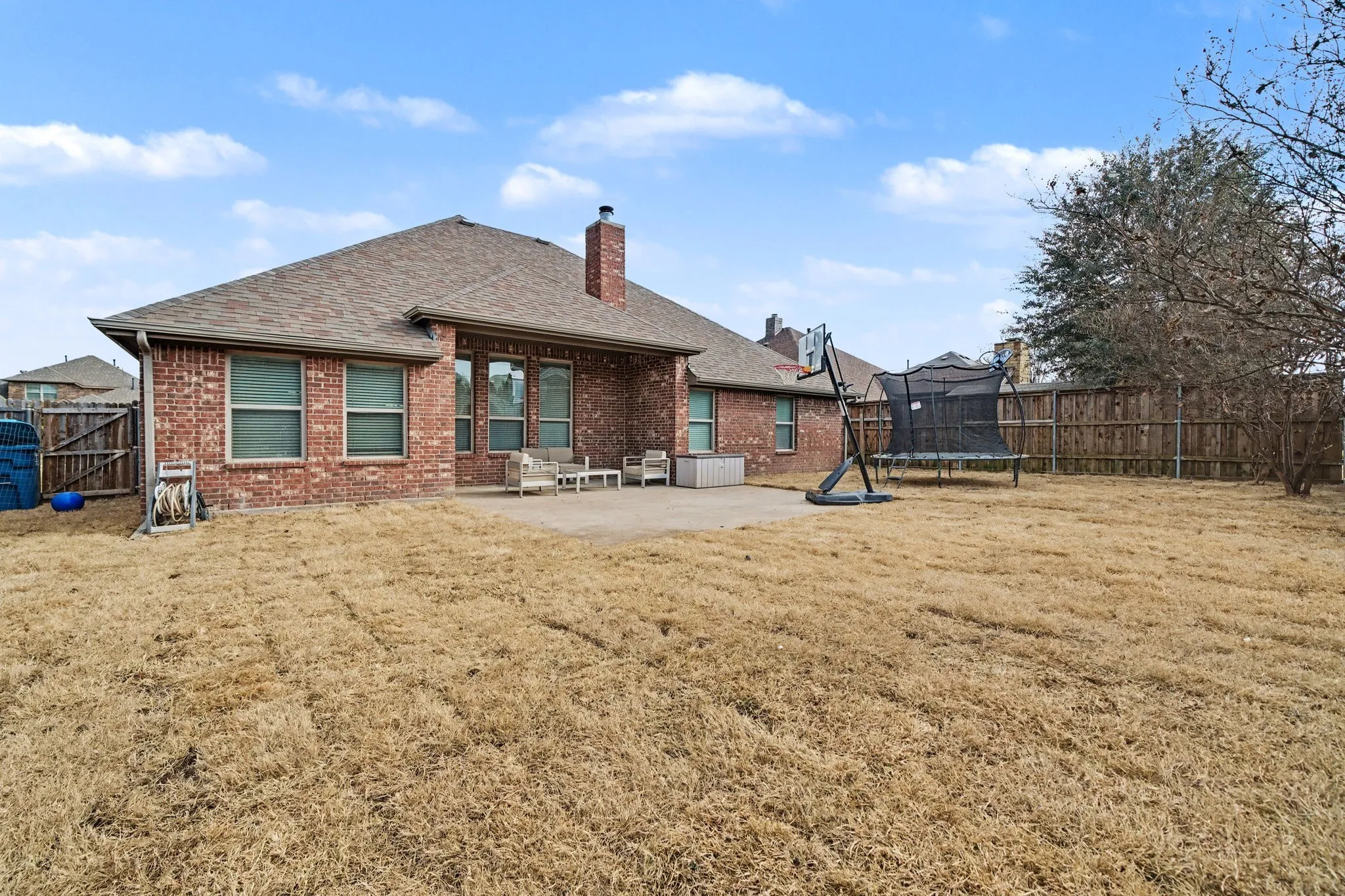 Rear view of property with a fenced backyard, brick siding, a patio area, a chimney, and a trampoline