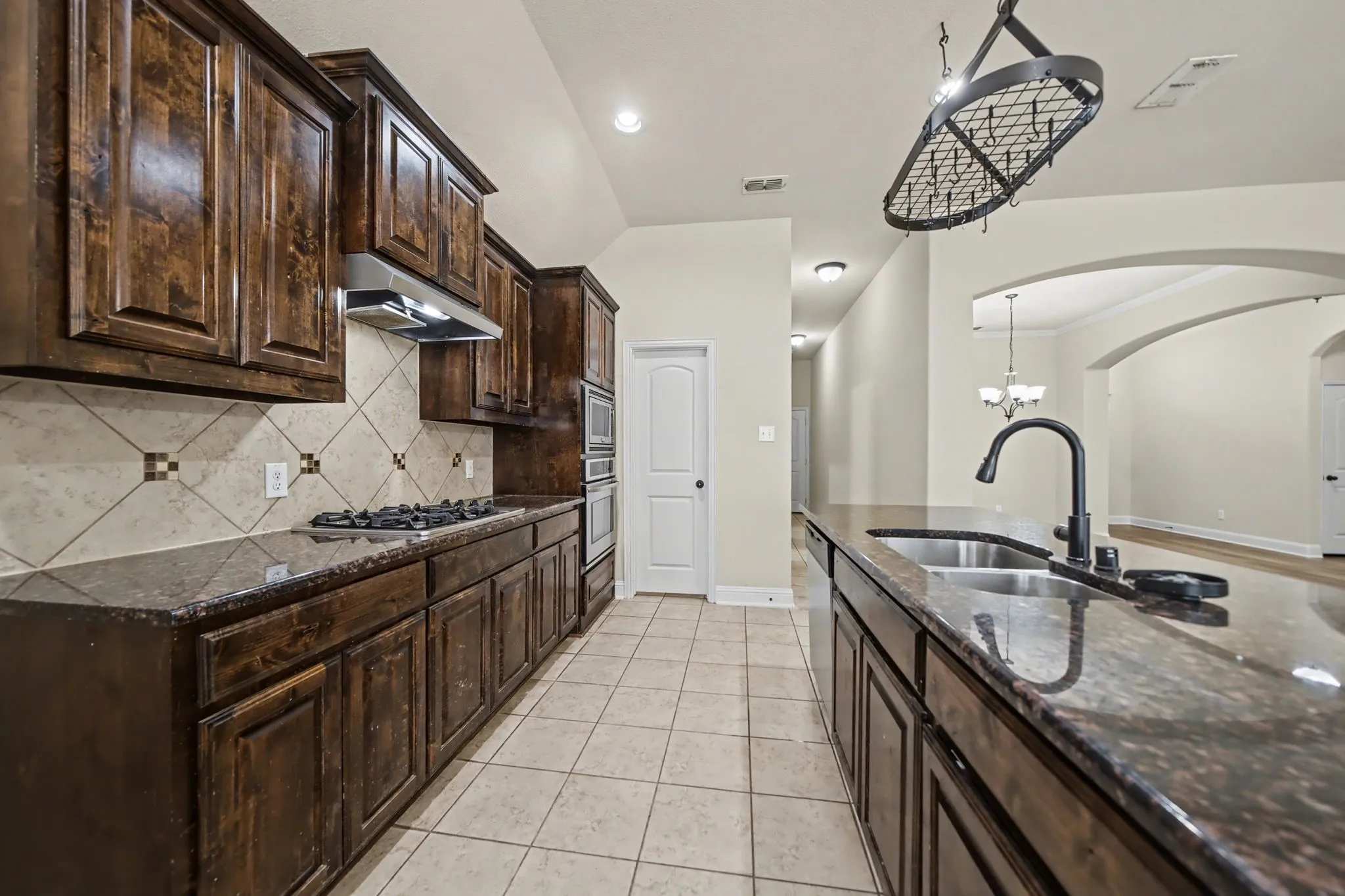 Kitchen with dark brown cabinetry, dark stone countertops, light tile patterned floors, decorative light fixtures, and recessed lighting