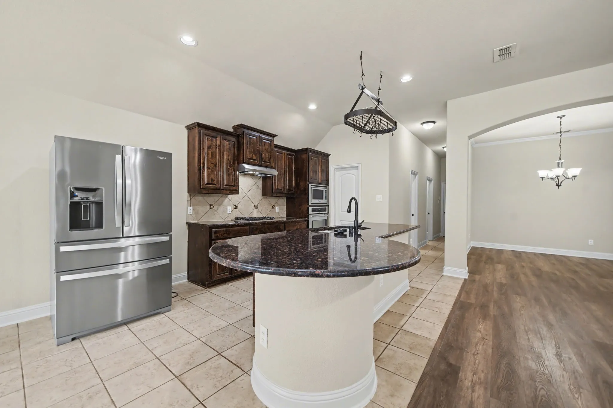 Kitchen featuring dark brown cabinetry, appliances with stainless steel finishes, dark stone countertops, light tile patterned flooring, and a kitchen island with sink