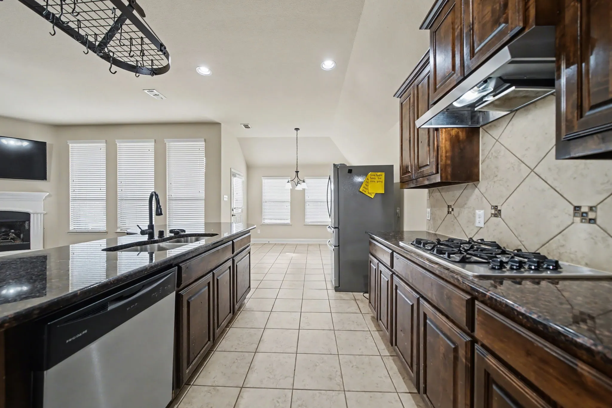 Kitchen with dark brown cabinets, dark stone countertops, stainless steel appliances, under cabinet range hood, and light tile patterned flooring