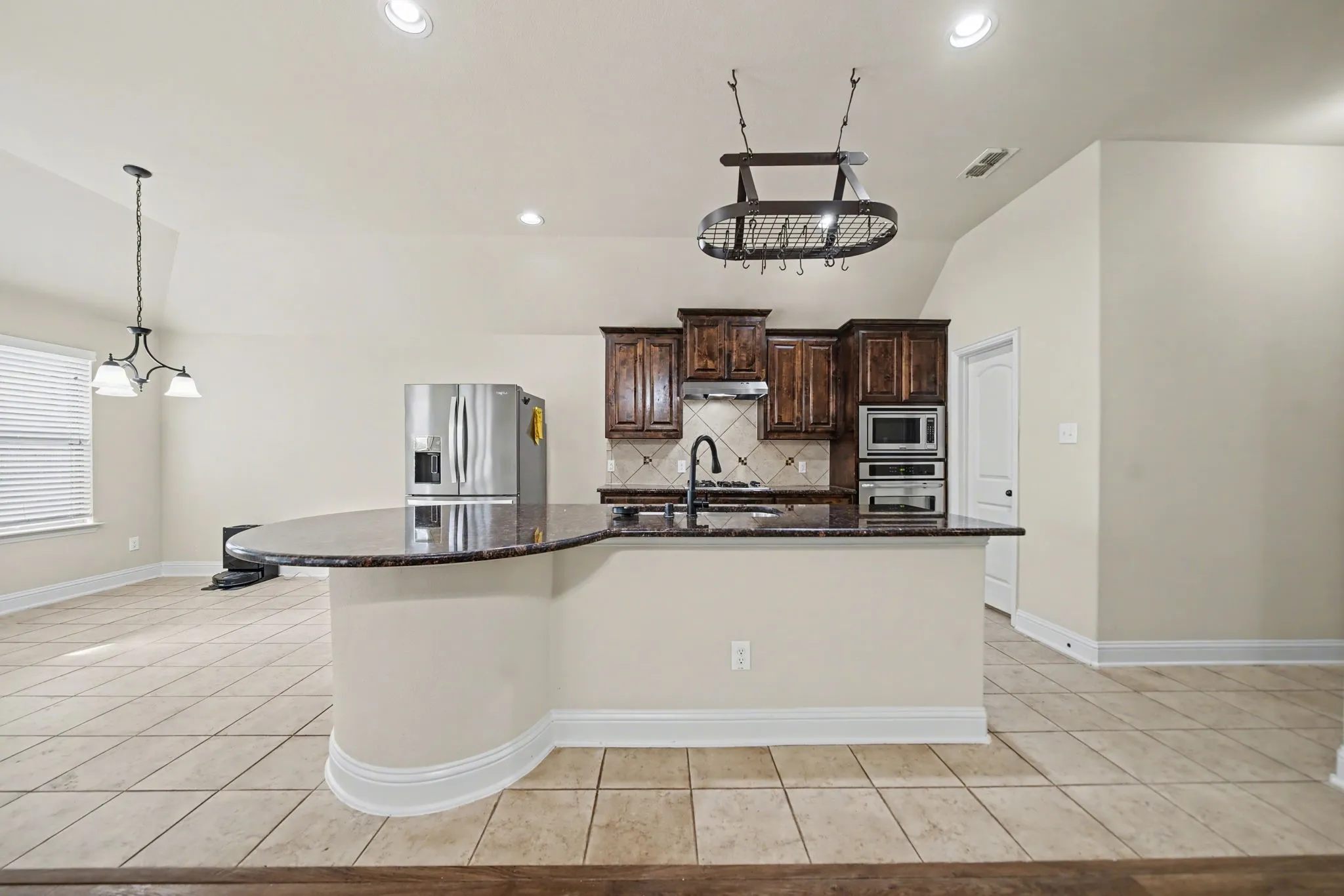 Kitchen featuring dark brown cabinets, lofted ceiling, tasteful backsplash, appliances with stainless steel finishes, and dark stone countertops