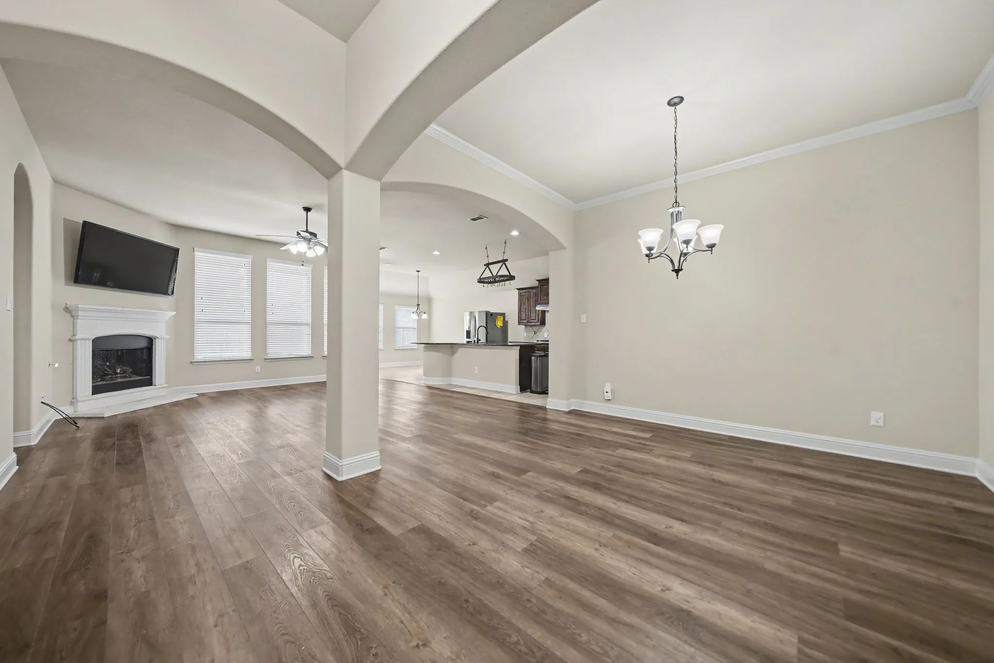 Unfurnished living room featuring a ceiling fan, a fireplace with raised hearth, arched walkways, a chandelier, and dark wood-style floors