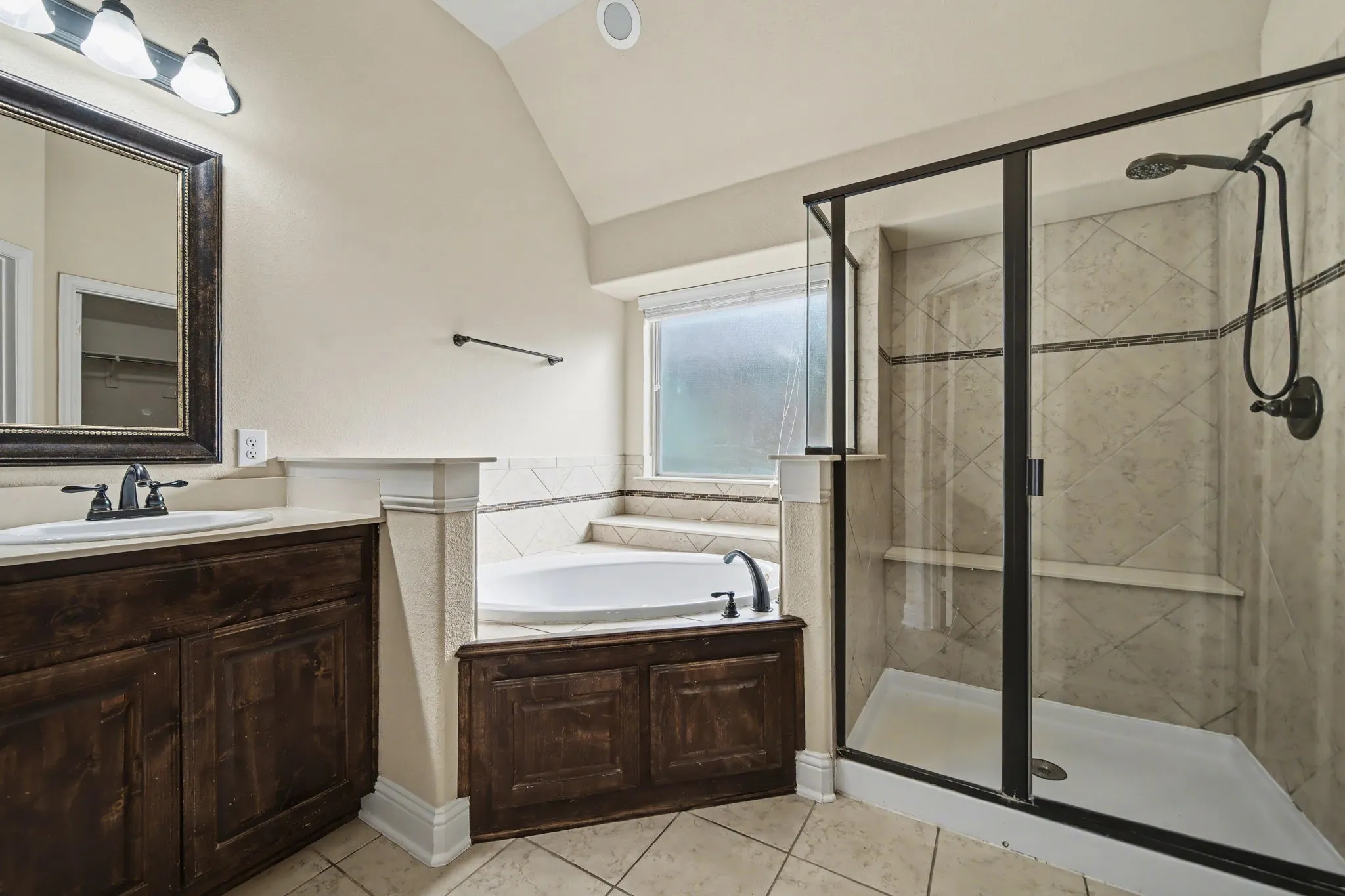 Bathroom featuring a garden tub, a stall shower, light tile patterned floors, vanity, and vaulted ceiling