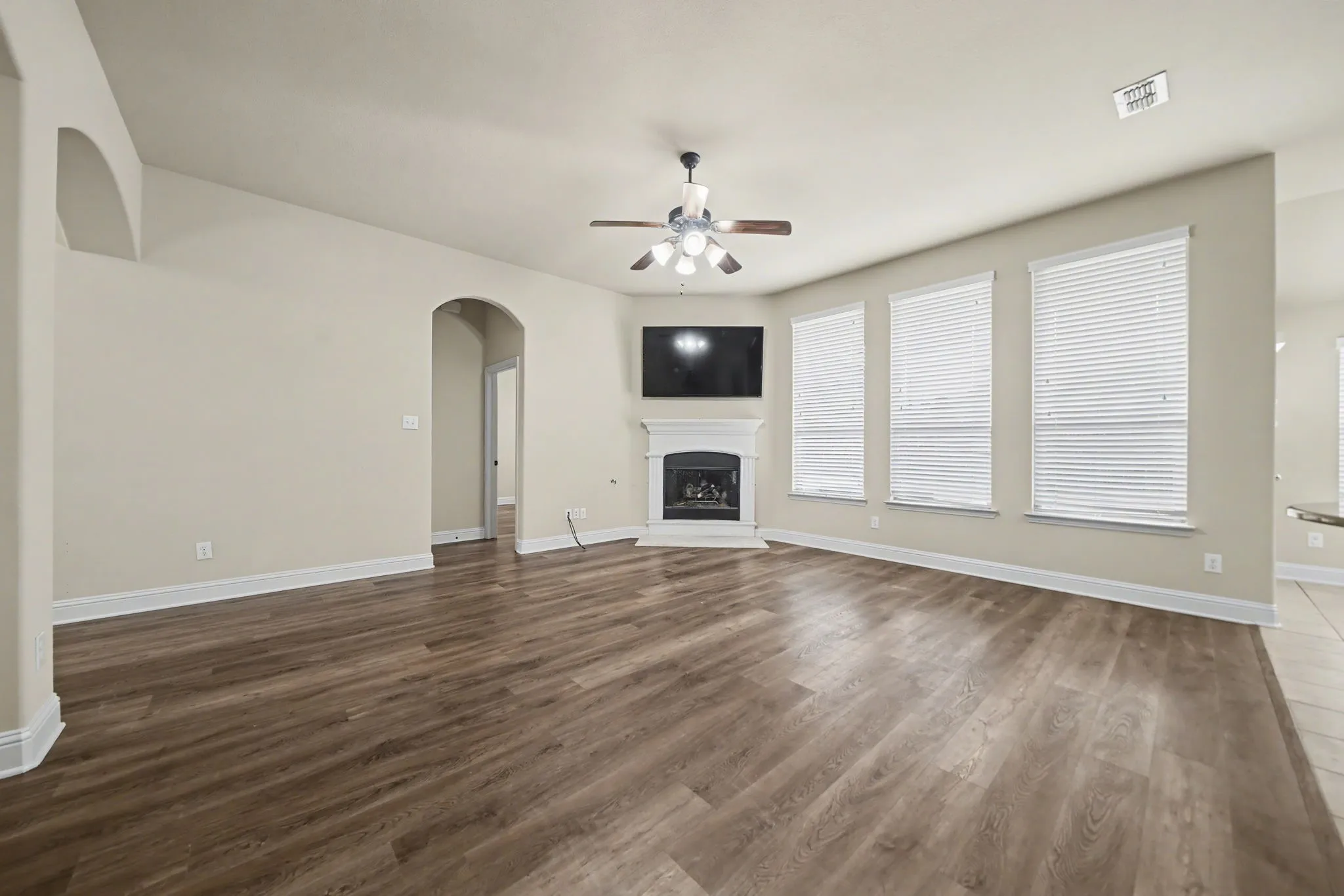 Unfurnished living room featuring a fireplace with raised hearth, arched walkways, dark wood-type flooring, and ceiling fan
