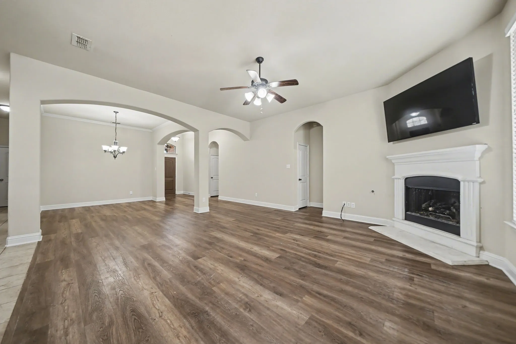 Unfurnished living room featuring a fireplace with raised hearth, a ceiling fan, dark wood finished floors, and a chandelier