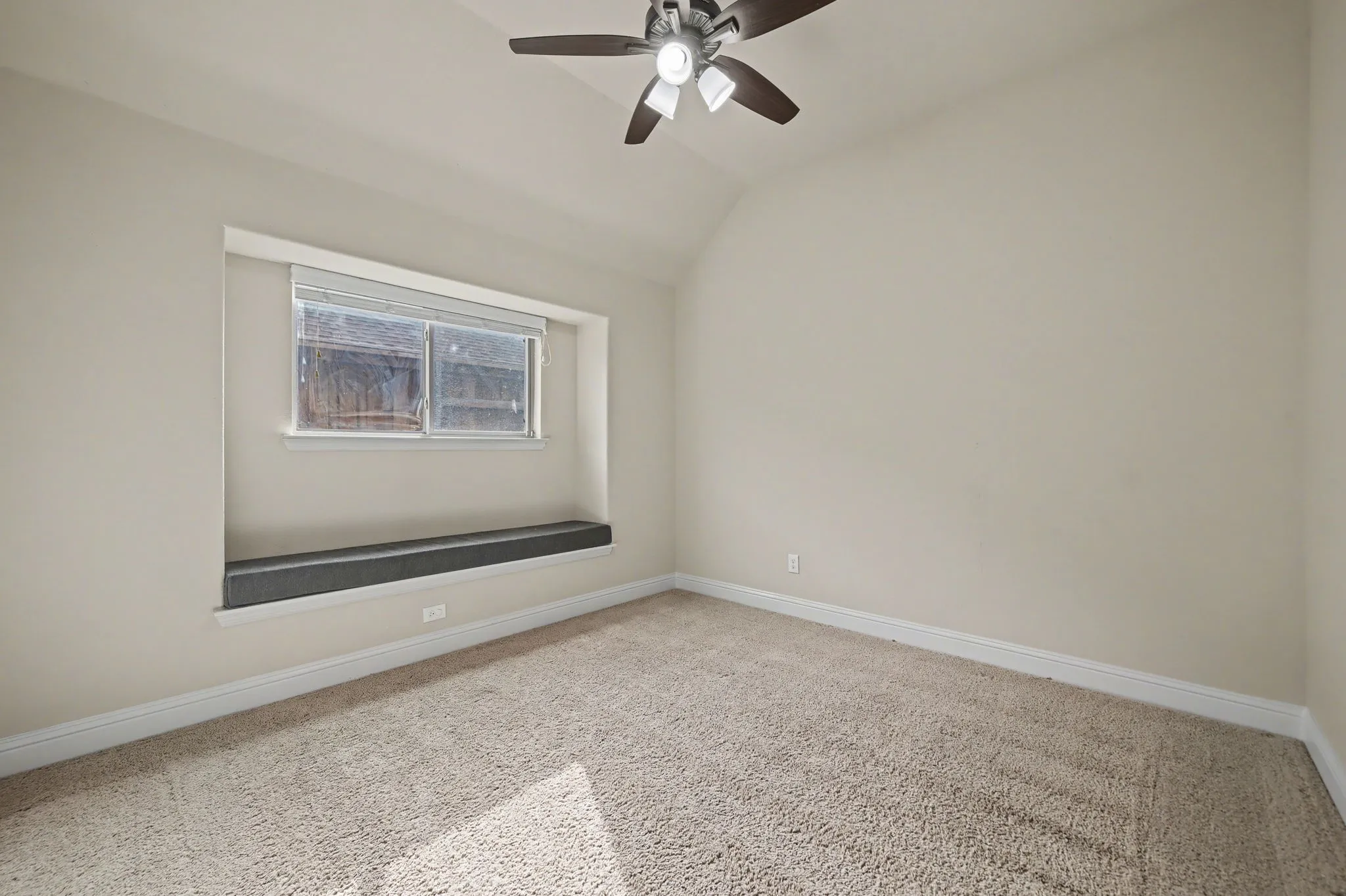 Carpeted spare room featuring vaulted ceiling and ceiling fan