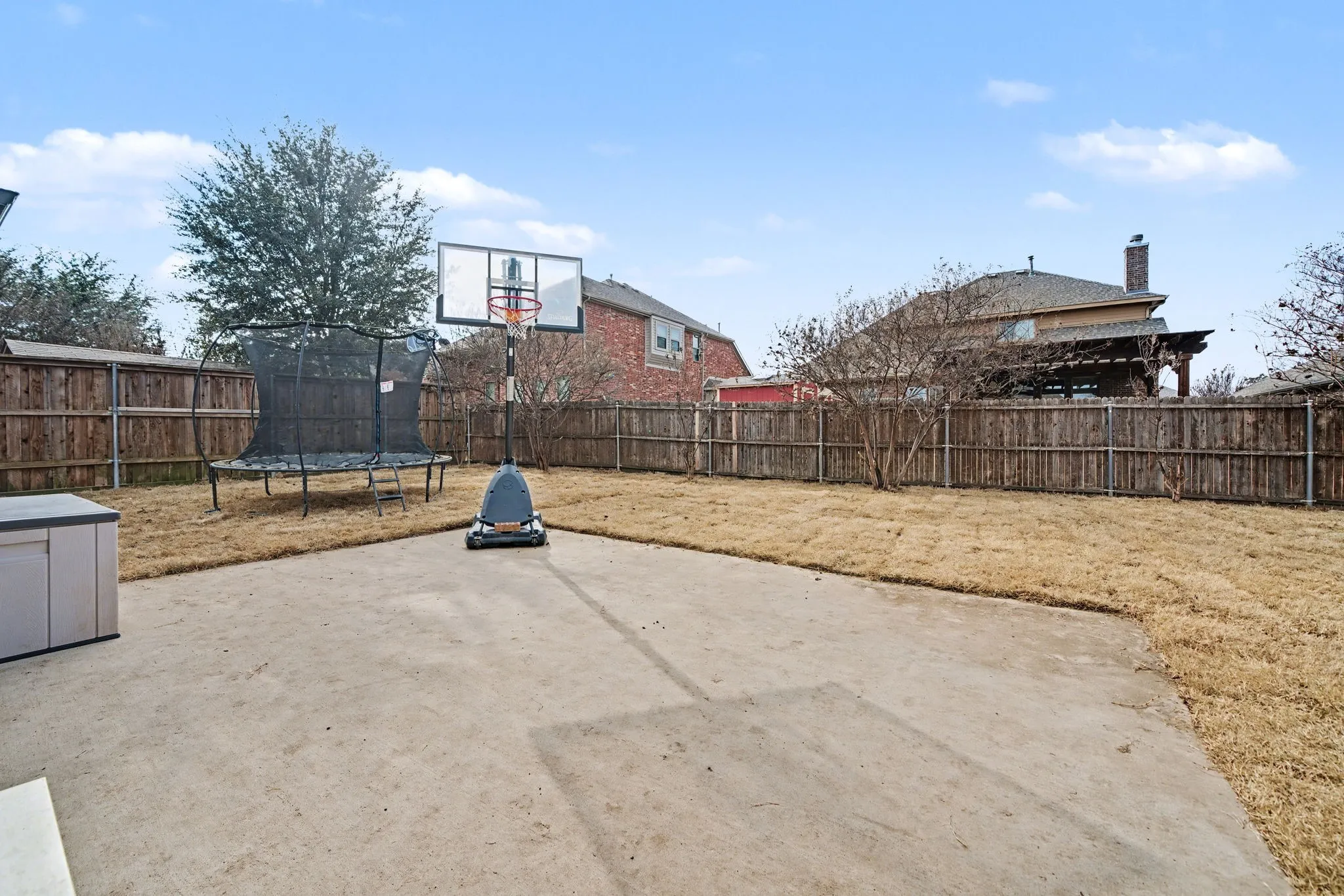 View of basketball court with a trampoline, a fenced backyard, and a patio area