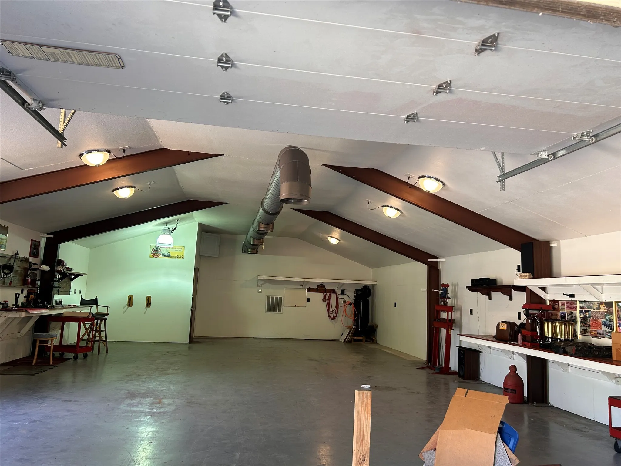 Expansive garage space featuring a concrete floor, exposed wood beams, and multiple ceiling-mounted light fixtures