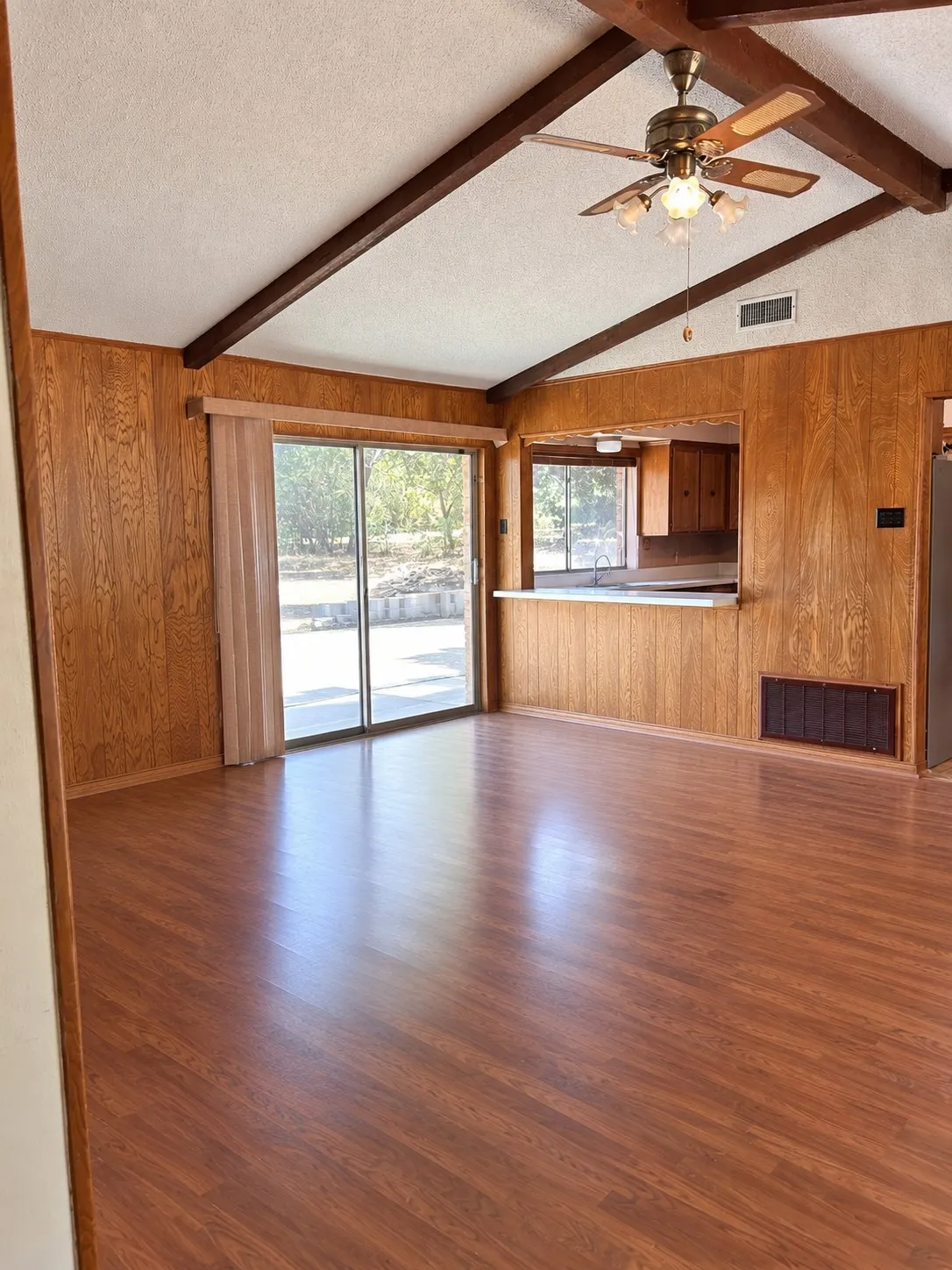 Vaulted ceiling with exposed wood beams, wood-finish flooring, wood paneling, sliding glass door, and a pass-through counter