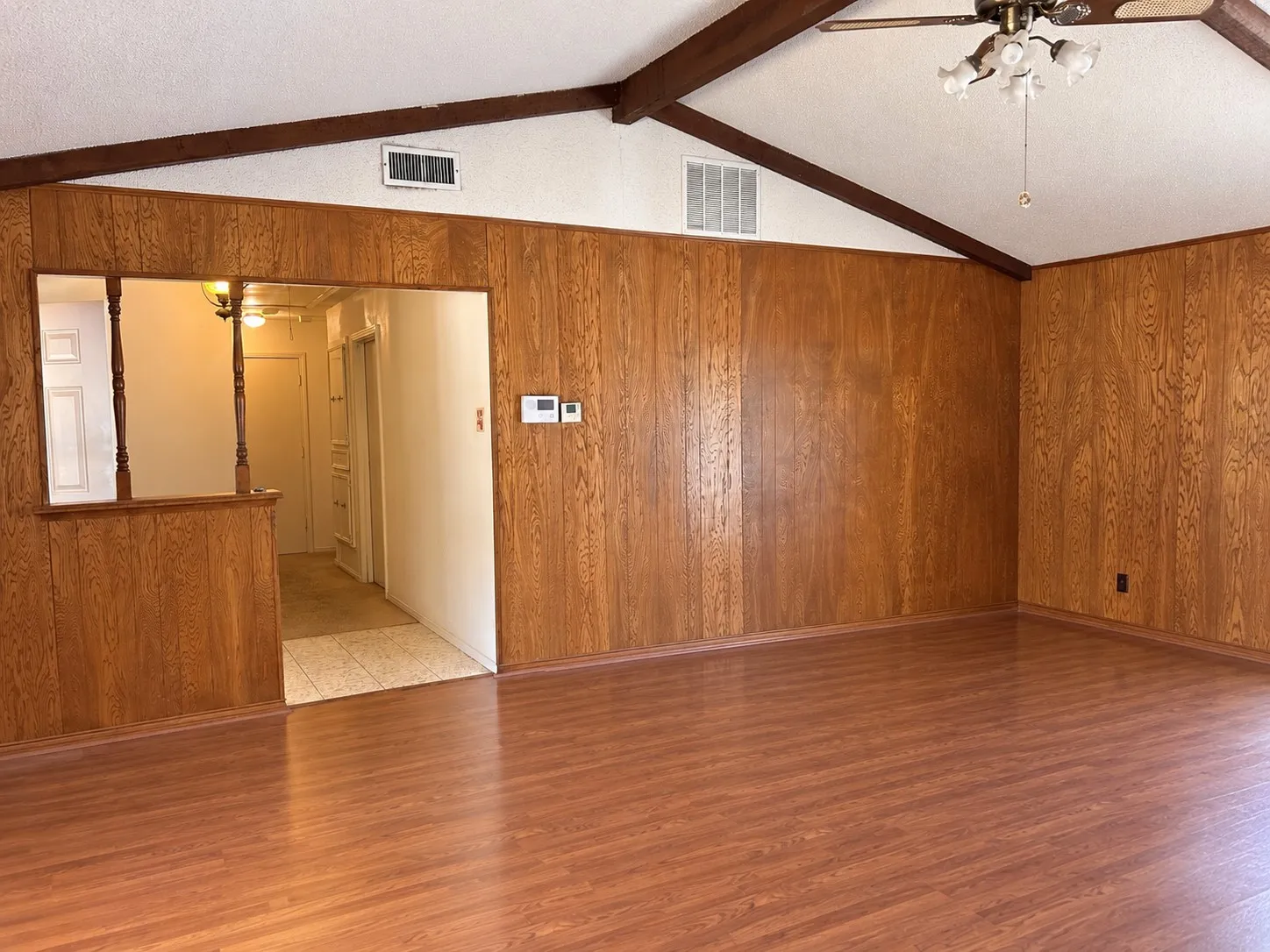 Vaulted ceiling with exposed wood beams, wood-finish flooring, wood-paneled walls, and a ceiling fan with integrated lighting
