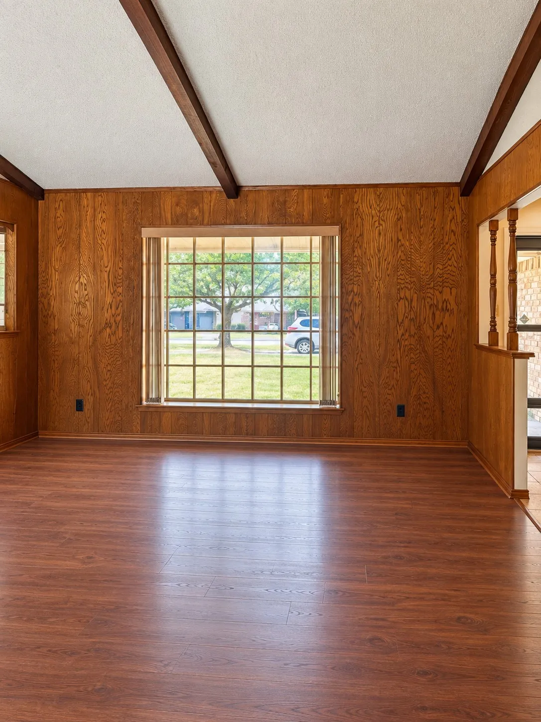 Vaulted ceiling with exposed wood beams, wood-finish flooring, wood paneling, and a large window with grid pattern
