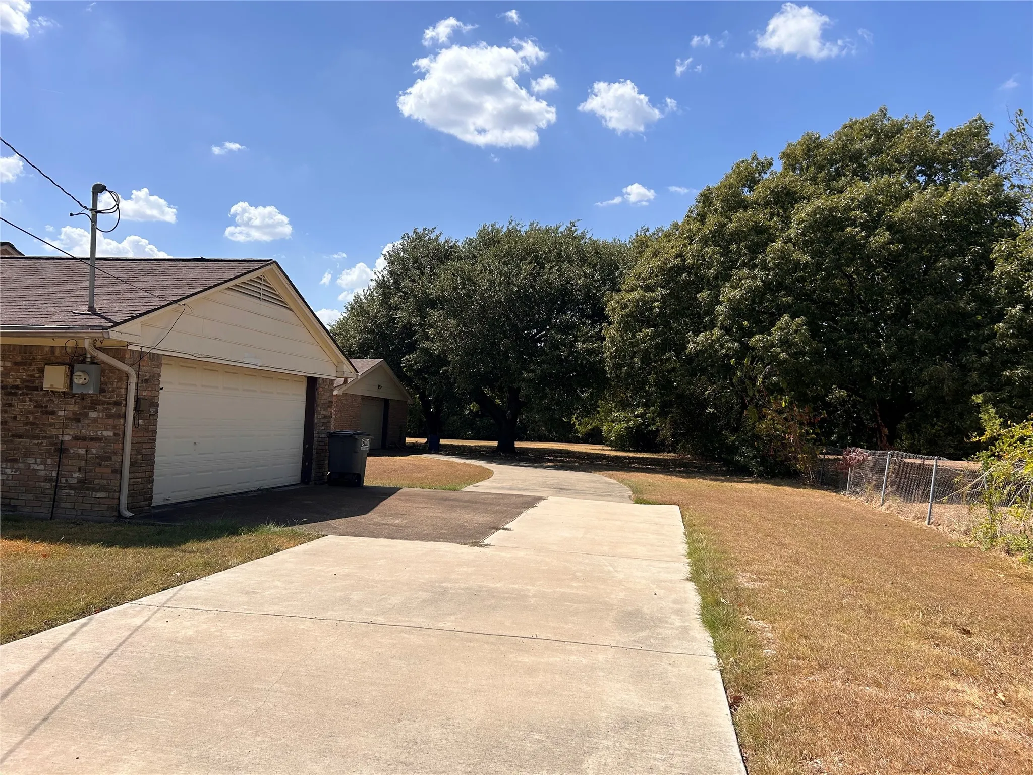 Brick exterior with an attached garage, featuring a concrete driveway and mature trees