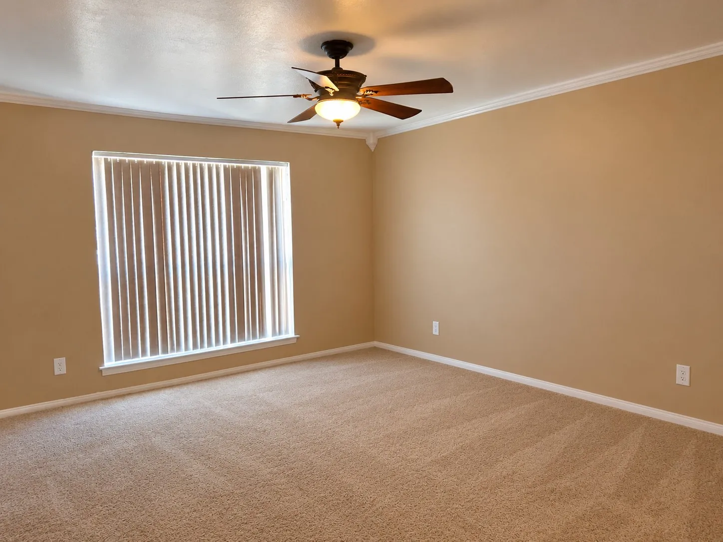 Neutral-toned carpeted flooring, a ceiling fan with integrated lighting, crown molding, and a window with vertical blinds