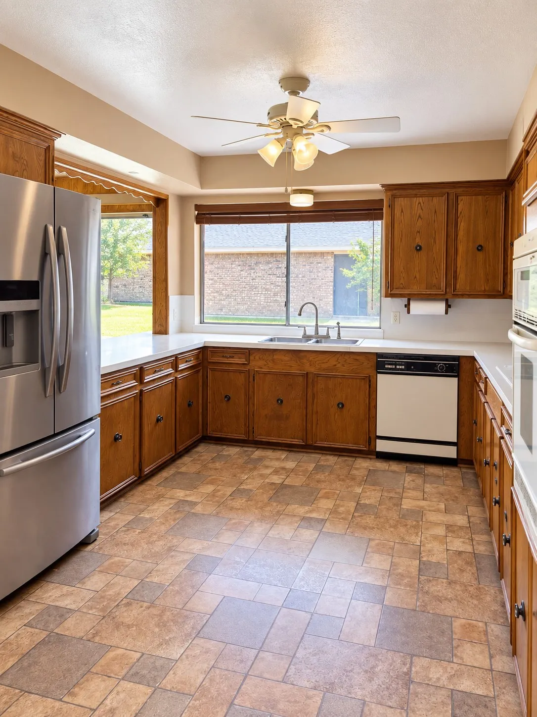 Kitchen featuring wood cabinetry, white countertops, a stainless steel refrigerator, a double basin sink, and patterned floor tile
