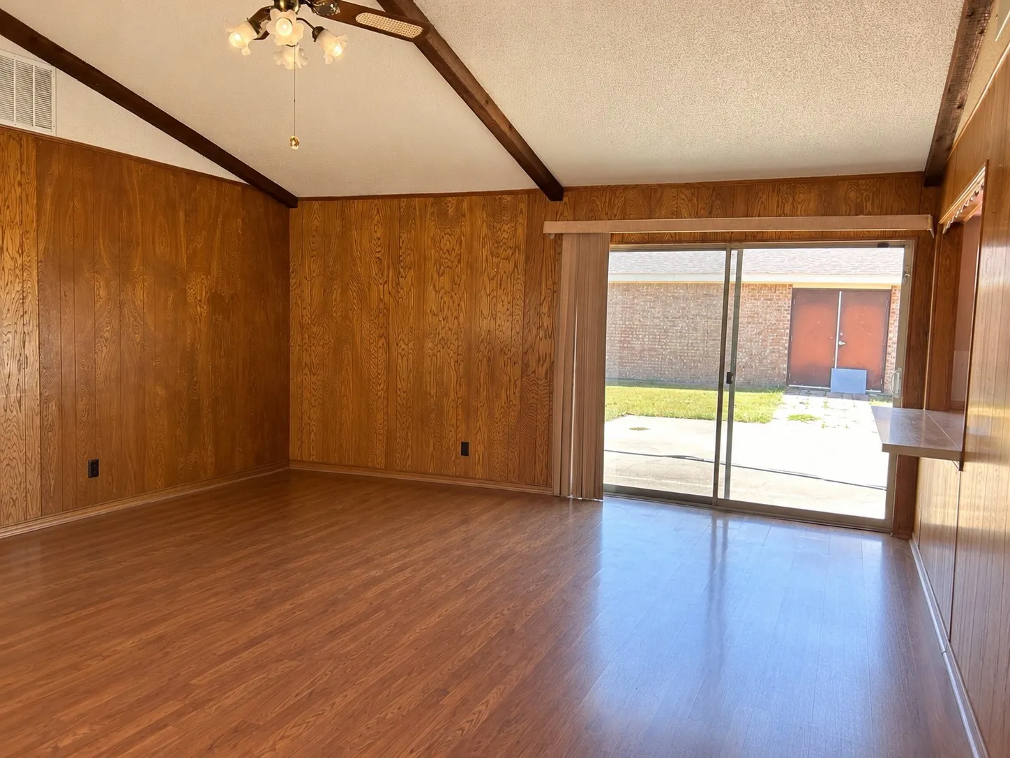 Vaulted ceiling with exposed wood beams, wood-finish flooring, wood paneling, sliding glass doors, and a built-in shelf