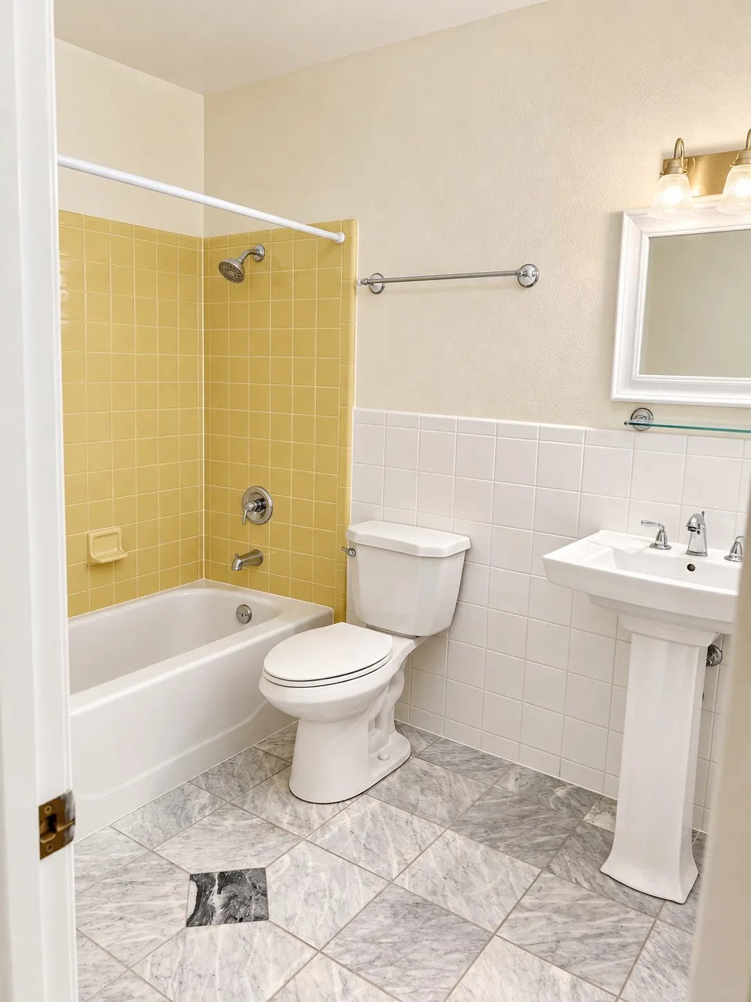 Pedestal sink, wall-mounted mirror, two-light vanity fixture, tiled shower surround, and gray and black tiled flooring