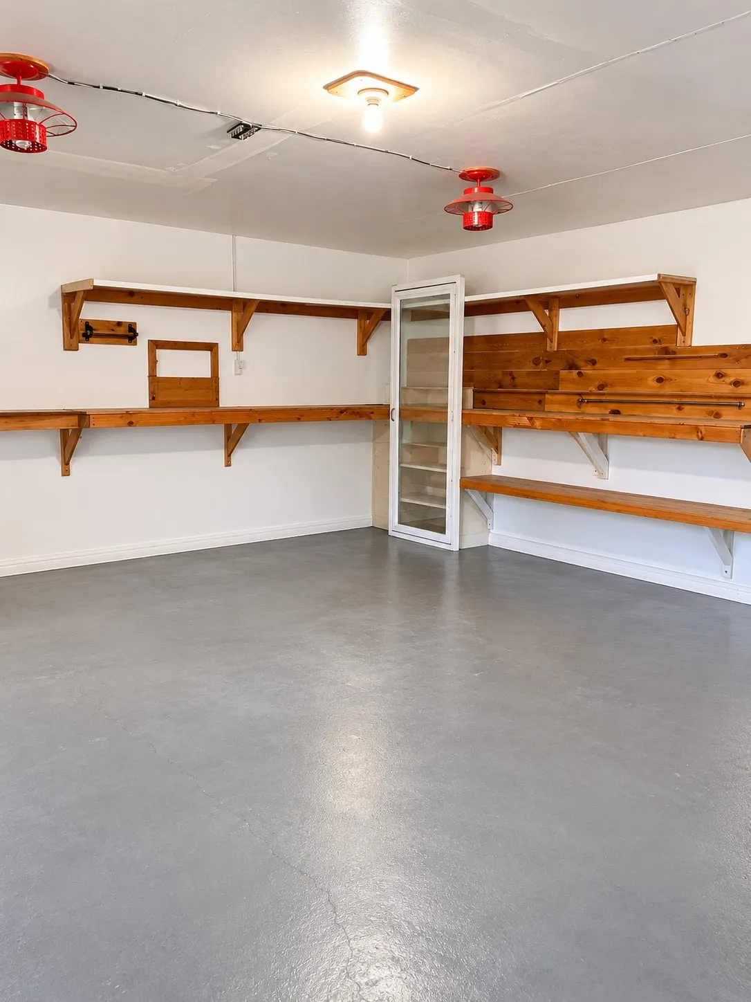 Garage space with a durable gray floor coating, extensive wooden shelving, built-in cabinetry, and ceiling-mounted lighting fixtures