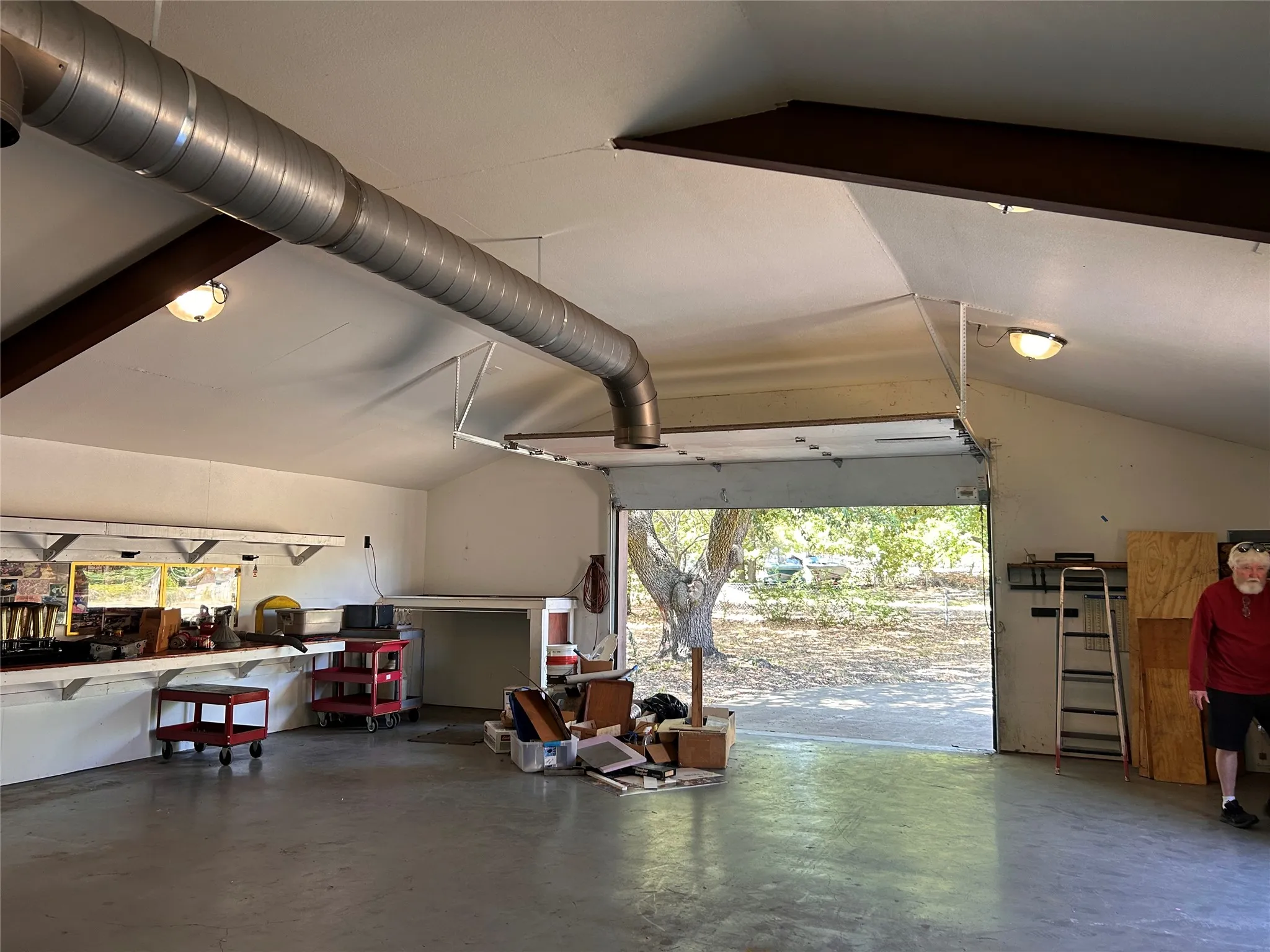 Spacious garage with exposed beam ceiling, built-in workbench, overhead lighting, and an open garage door