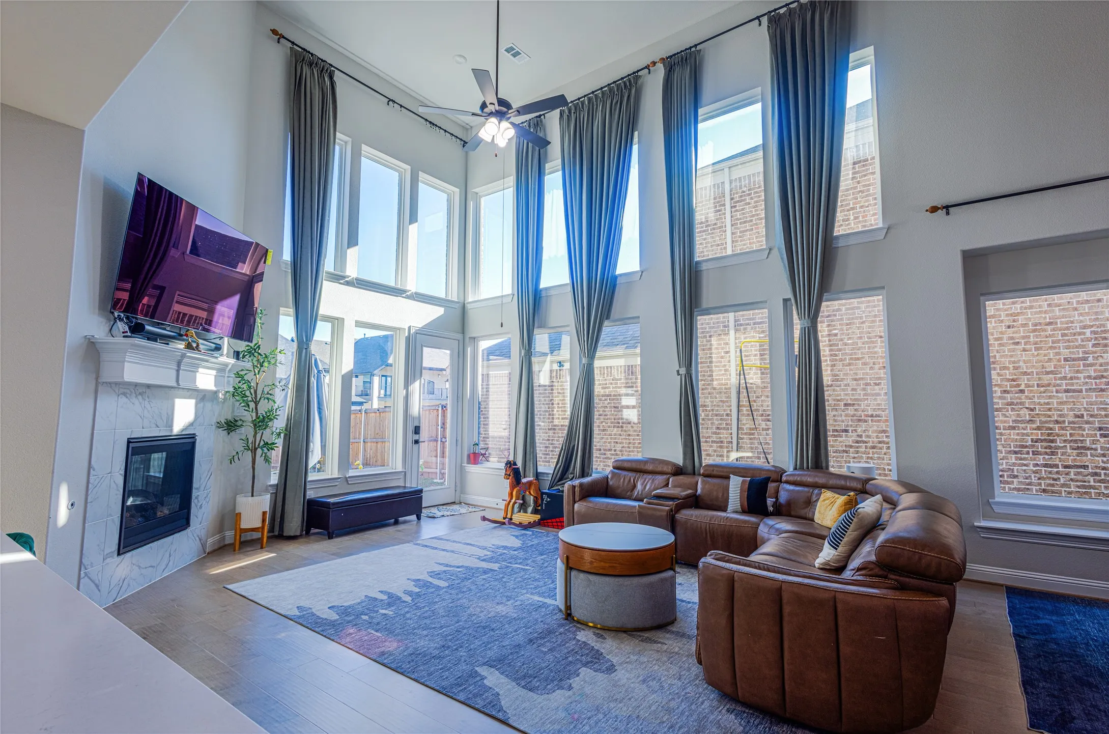 Living room featuring a premium fireplace, a ceiling fan, plenty of natural light, wood finished floors, and a high ceiling