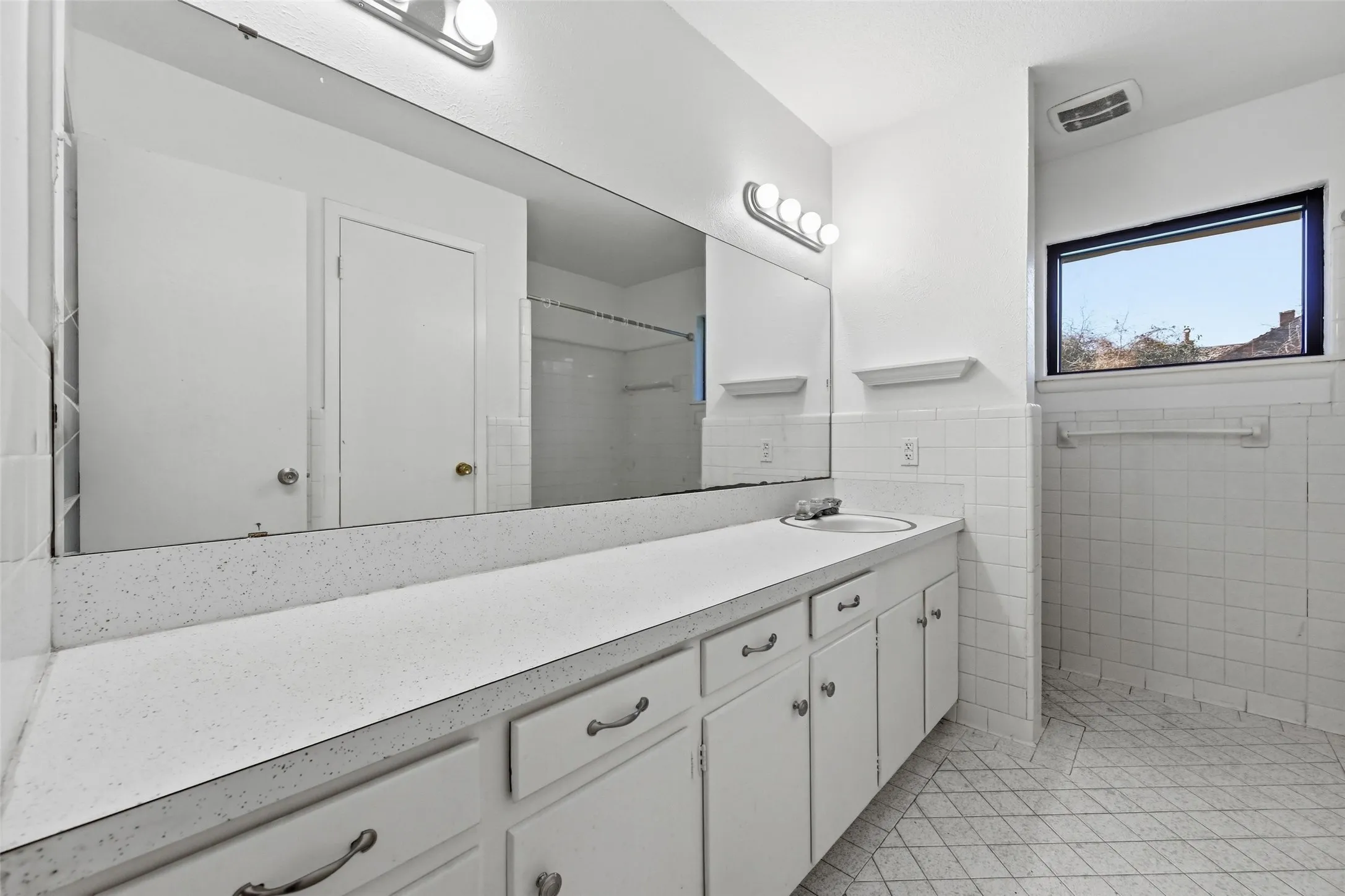 Bathroom featuring vanity, light tile patterned floors, a shower, tile walls, and a wainscoted wall