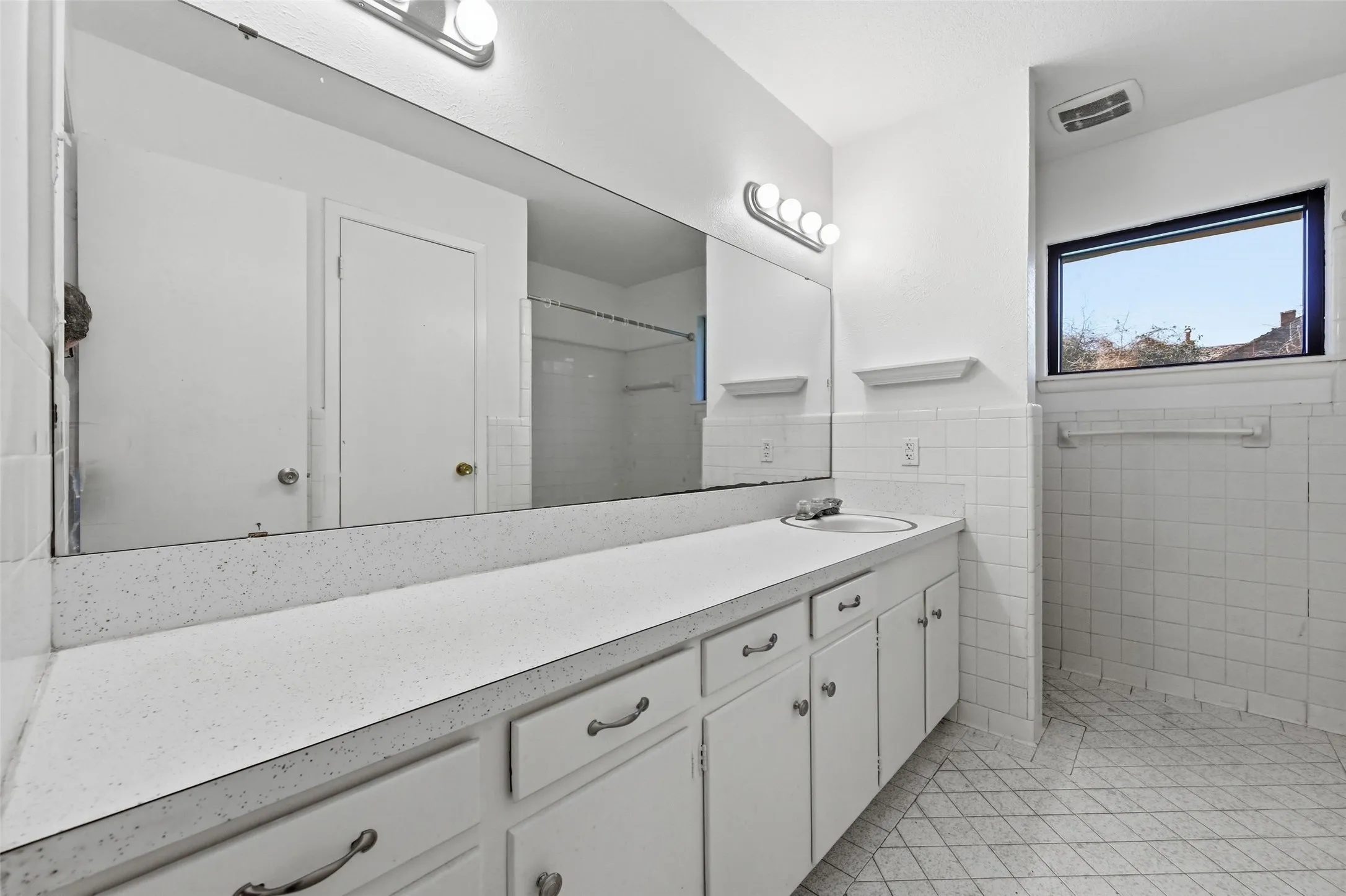 Full bathroom featuring vanity, light tile patterned floors, tile walls, a shower, and a wainscoted wall