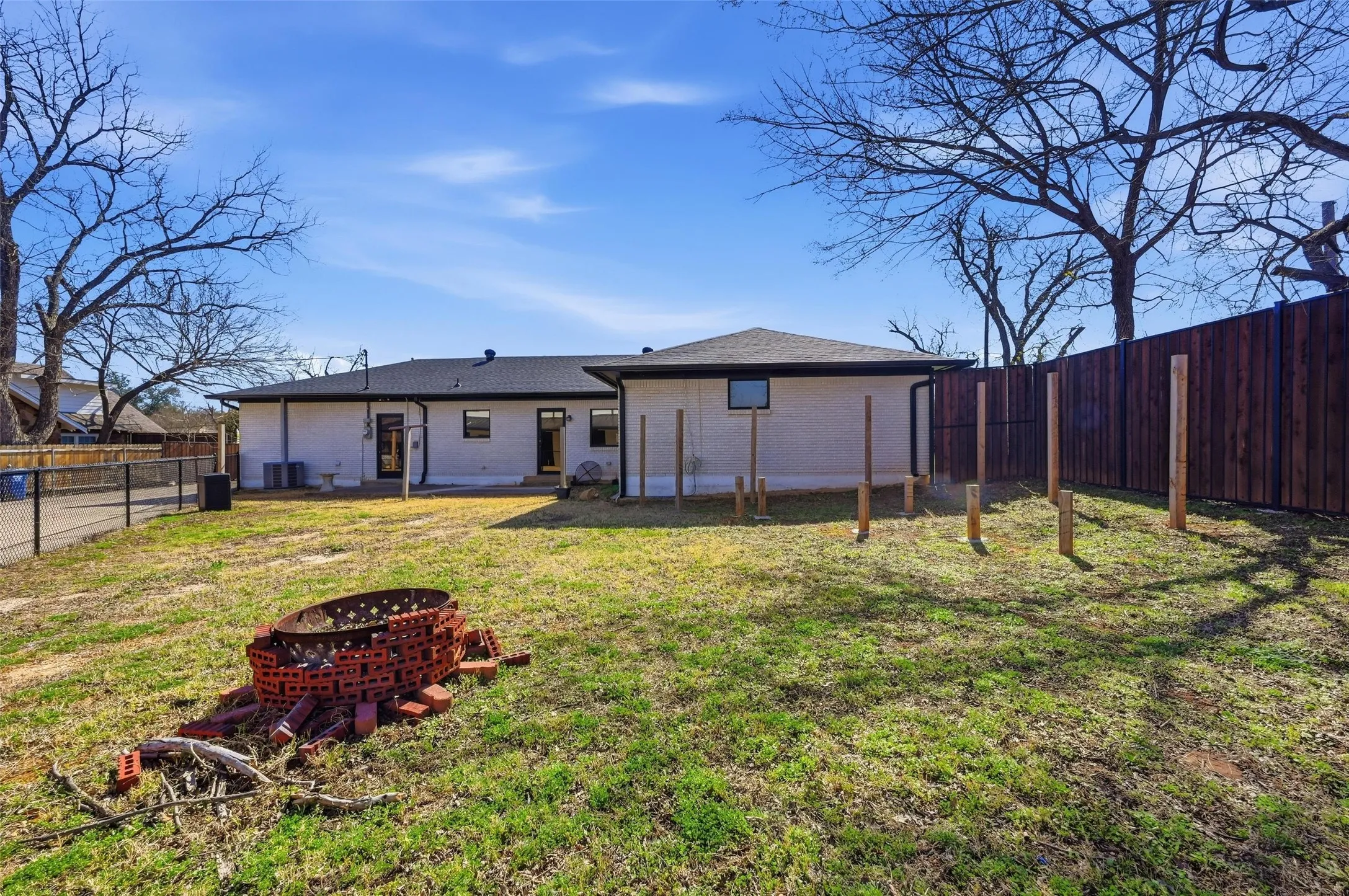 Back of house featuring a fenced backyard, brick siding, a fire pit, and a patio