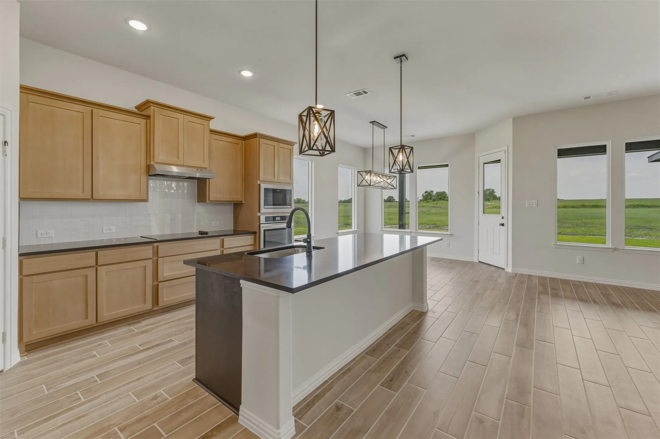 Expansive kitchen featuring a large island with a dark countertop and integrated sink, light wood cabinetry, built-in stainless steel appliances, and a white subway tile backsplash