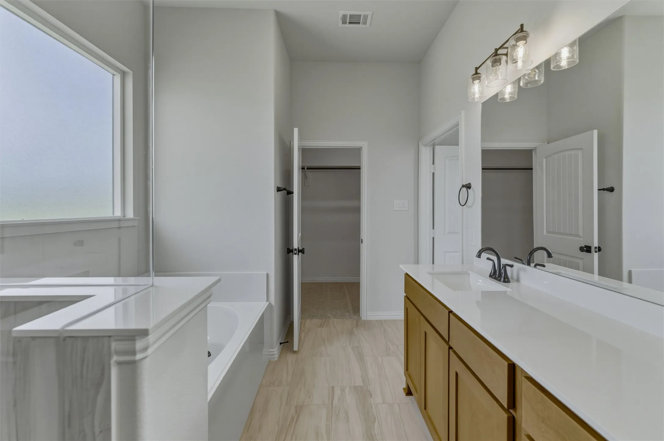 Spacious bathroom featuring a double vanity with ample counter space, a large soaking tub with tile surround, and a generously sized window providing natural light