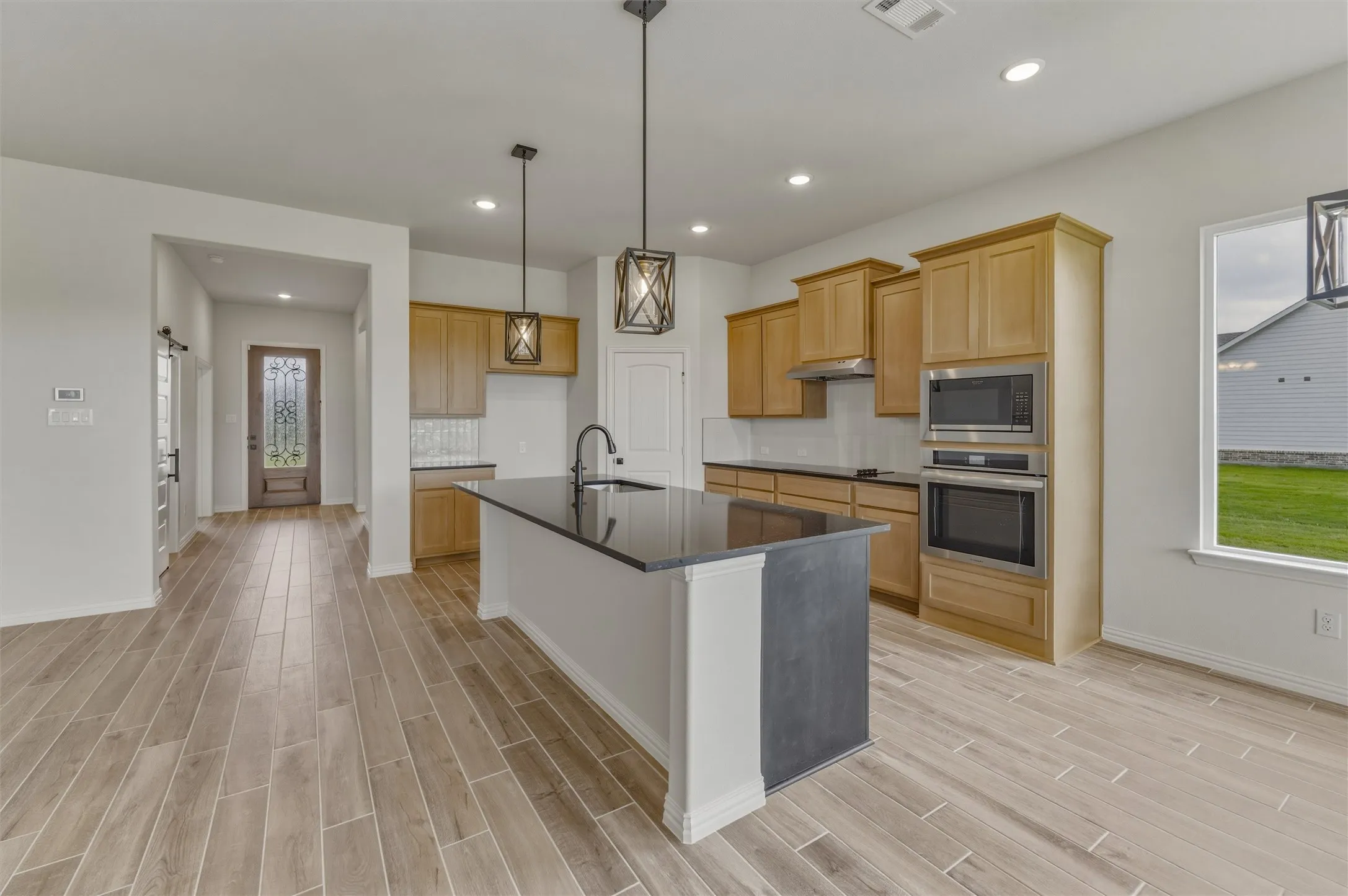 Kitchen featuring a dark countertop island with pendant lighting, wood-finish flooring, light wood cabinetry, stainless steel appliances, and recessed lighting