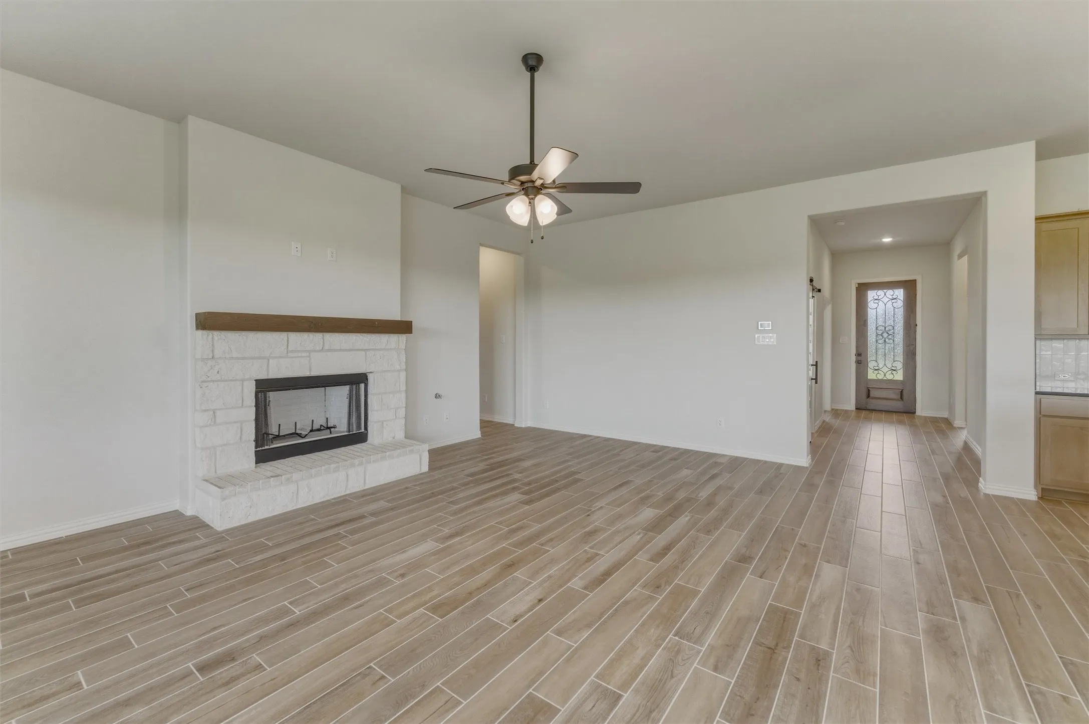 Spacious interior featuring wood-finish flooring throughout, a stone-faced fireplace with a wood mantel, and a ceiling fan