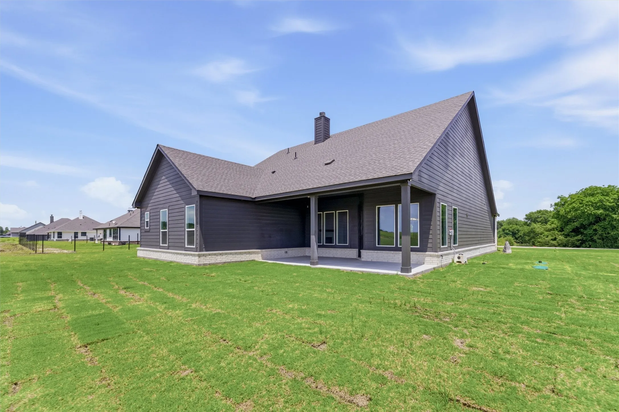 Modern home exterior featuring dark siding, a covered patio, multiple large windows, and a shingled roof