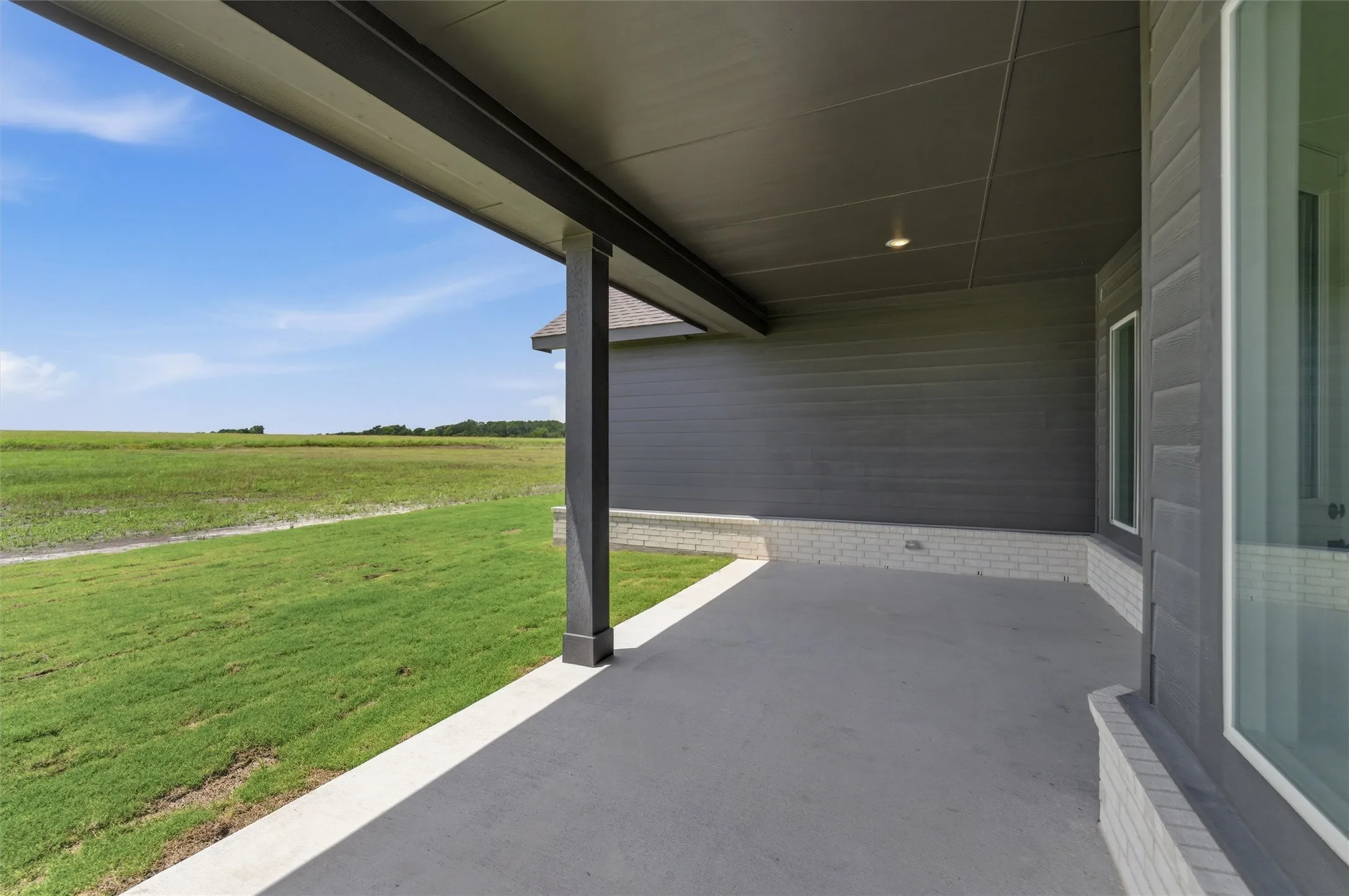 Covered patio with recessed lighting, featuring gray siding and light brick accents