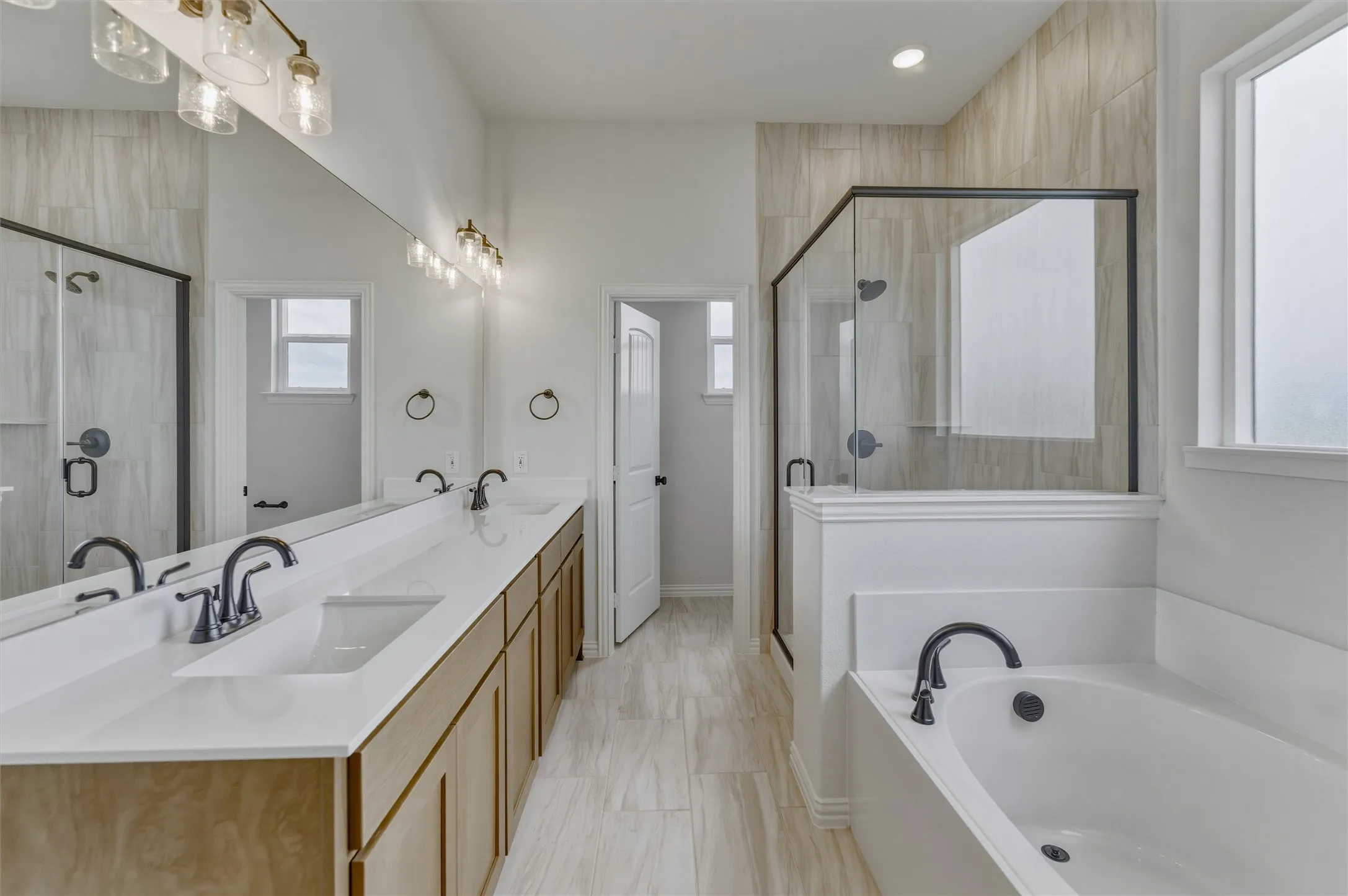 Contemporary bathroom featuring a dual vanity with undermount sinks, bronze finish fixtures, a built-in soaking tub, and a glass-enclosed shower with tiled walls