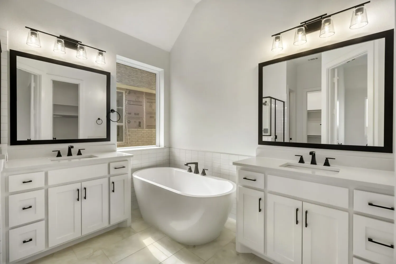 Bathroom with a freestanding tub, tile walls, two vanities, a walk in closet, and wainscoting