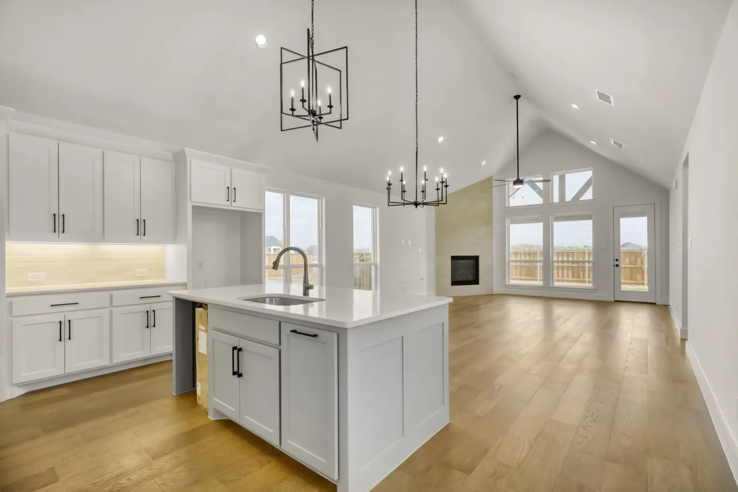 Kitchen featuring white cabinetry, a large fireplace, an island with sink, light wood-style floors, and a chandelier