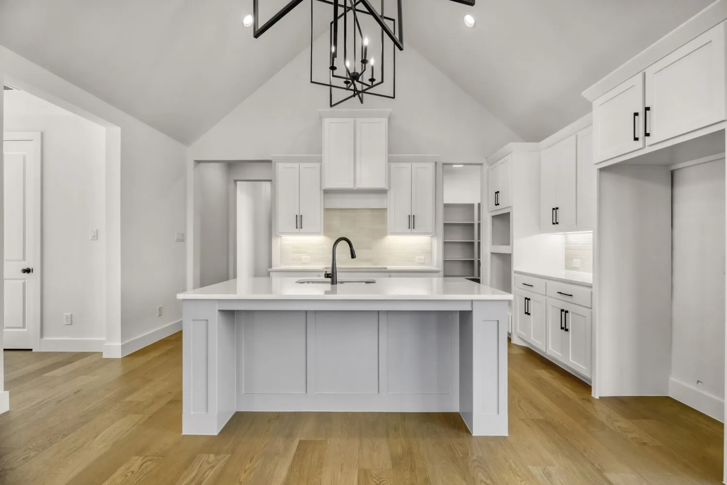 Kitchen featuring a high ceiling, white cabinetry, a center island with sink, decorative backsplash, and light wood-style floors