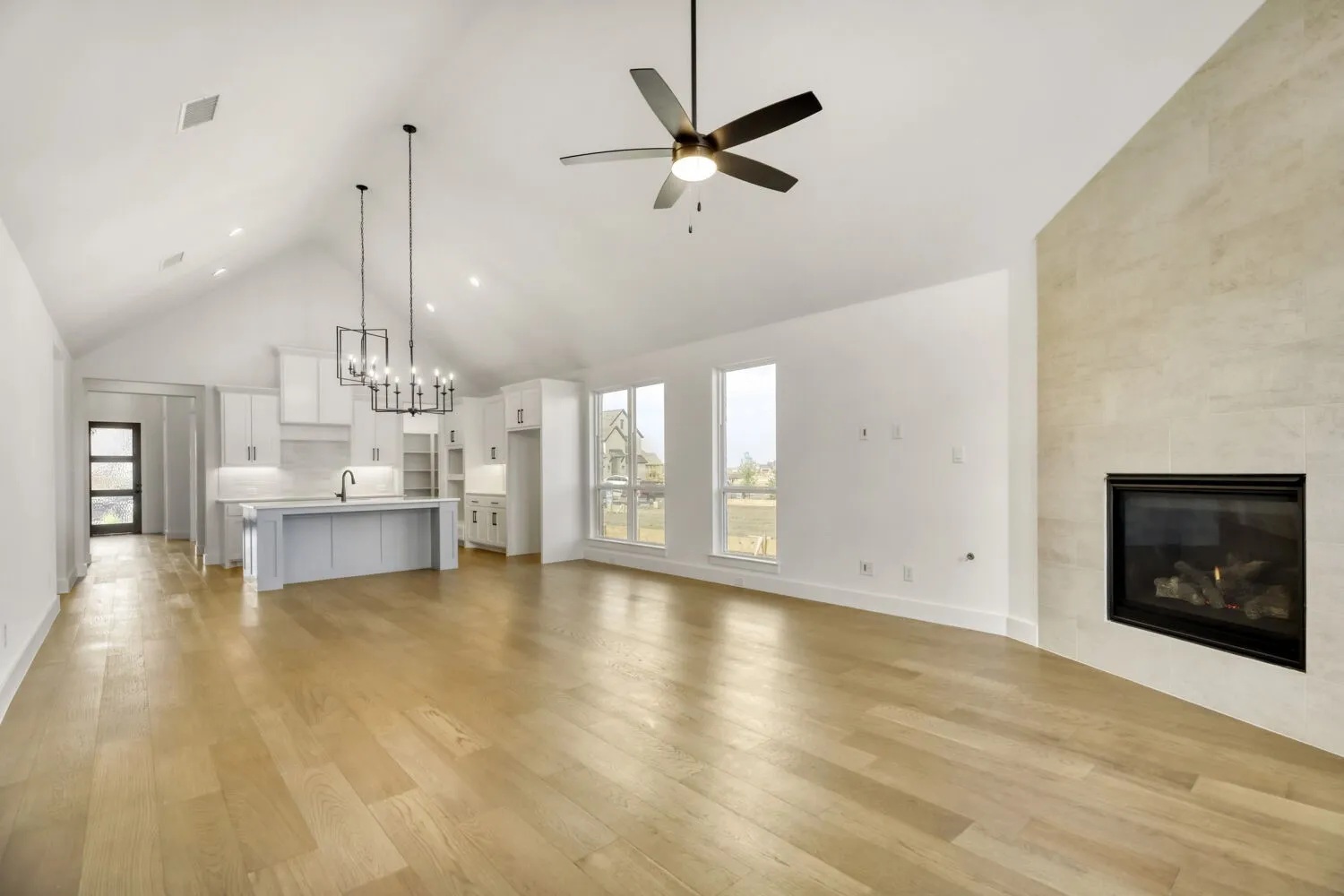 Unfurnished living room with a high ceiling, a tiled fireplace, light wood-style flooring, healthy amount of natural light, and a chandelier