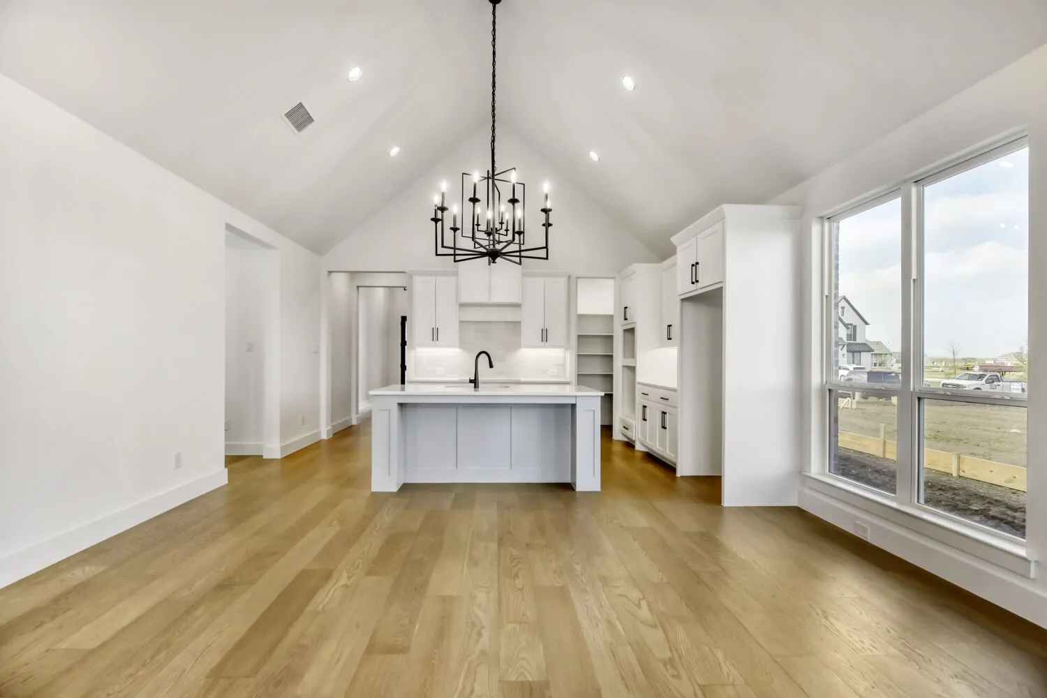 Kitchen featuring a high ceiling, an island with sink, white cabinets, hanging lights, and light wood-style flooring