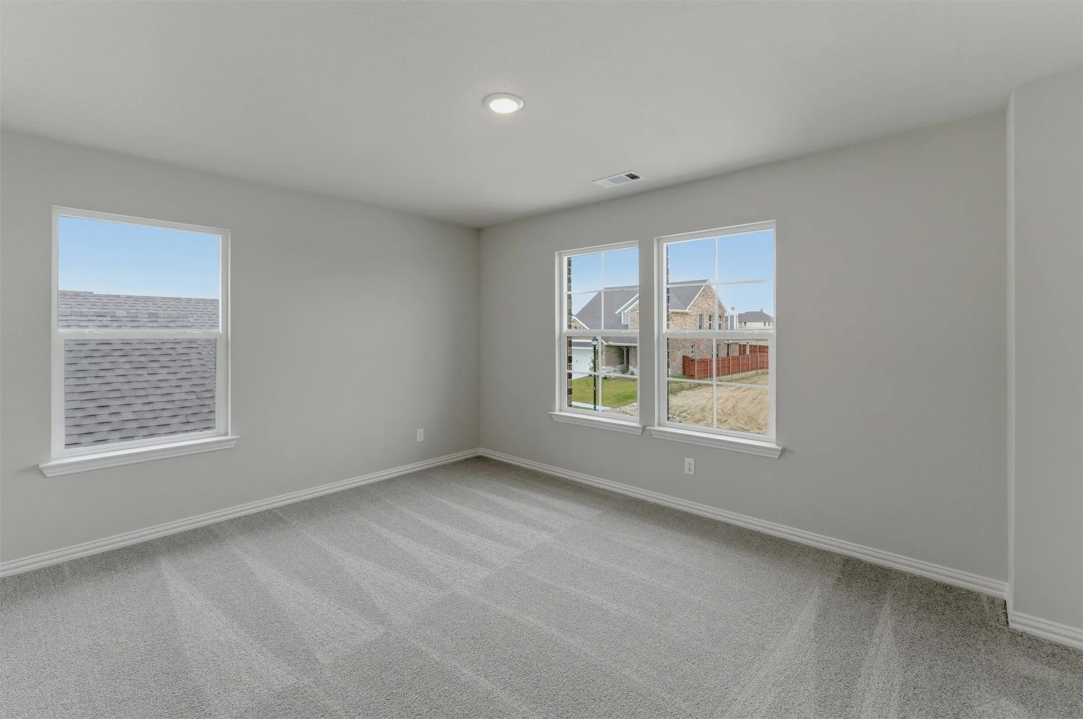 Spacious interior room featuring light gray carpeting, multiple windows with white trim, and recessed ceiling lighting