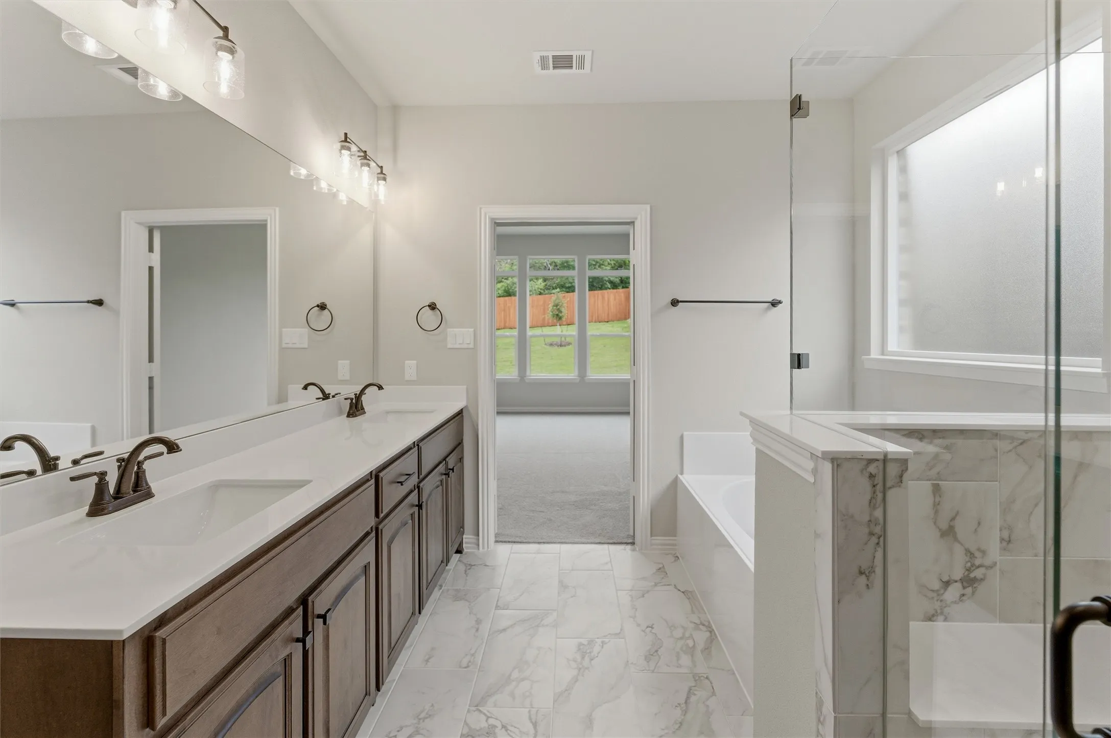 Bathroom featuring a dual vanity with dark wood cabinetry and white countertops, a large mirror with overhead lighting, a built-in bathtub, and a glass-enclosed shower with marble-look tile accents