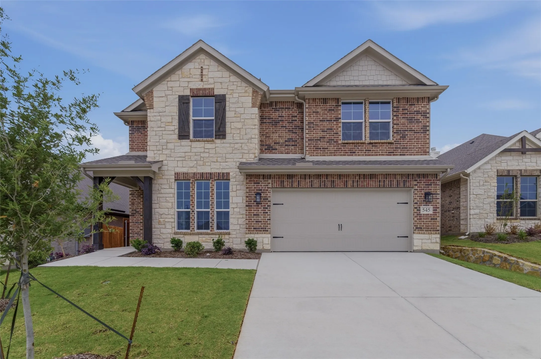Stone and brick facade with dark shutters, covered entry, and a two-car garage