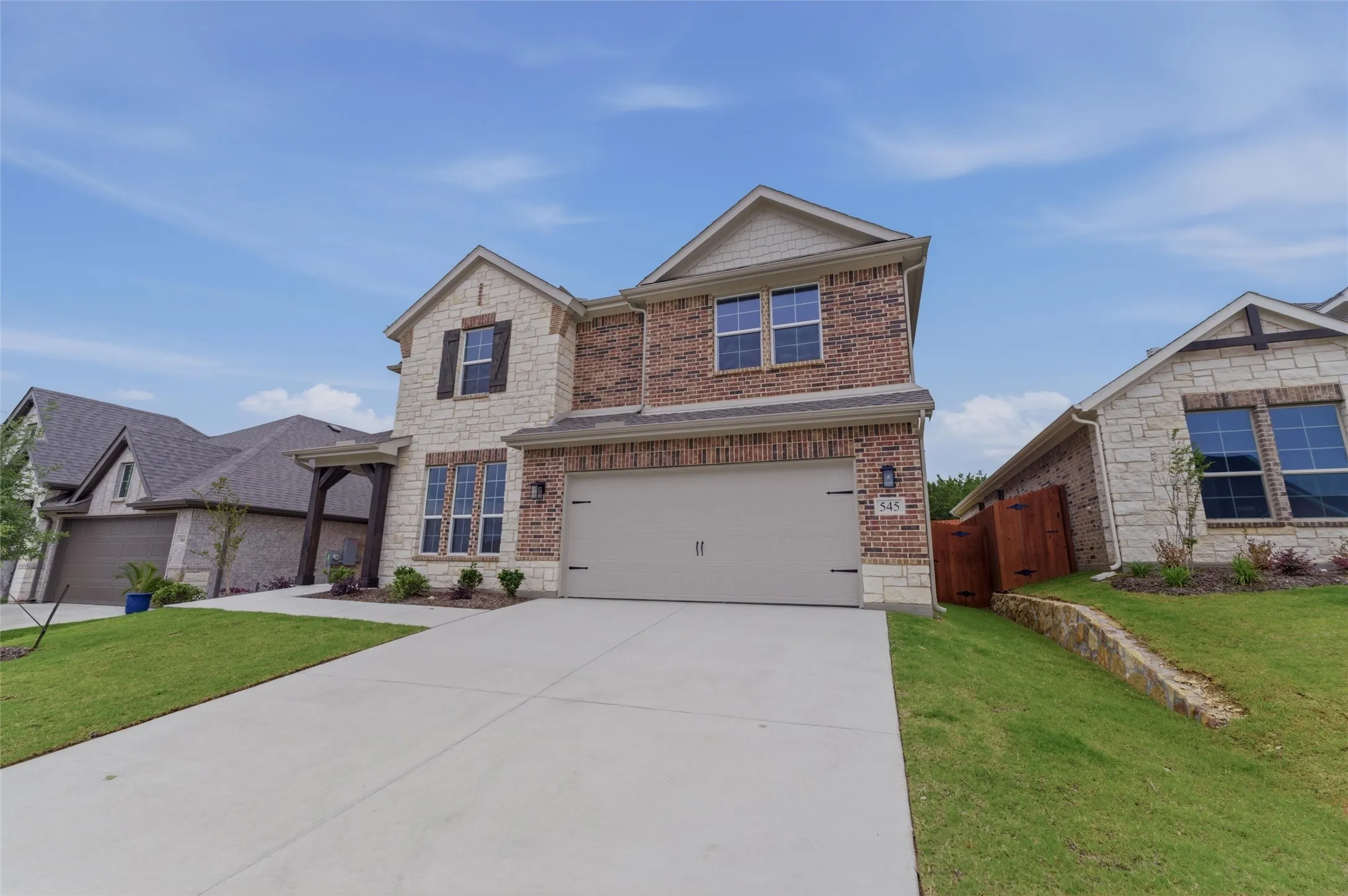 Two-story residence featuring a brick and stone facade, a two-car garage, and a concrete driveway