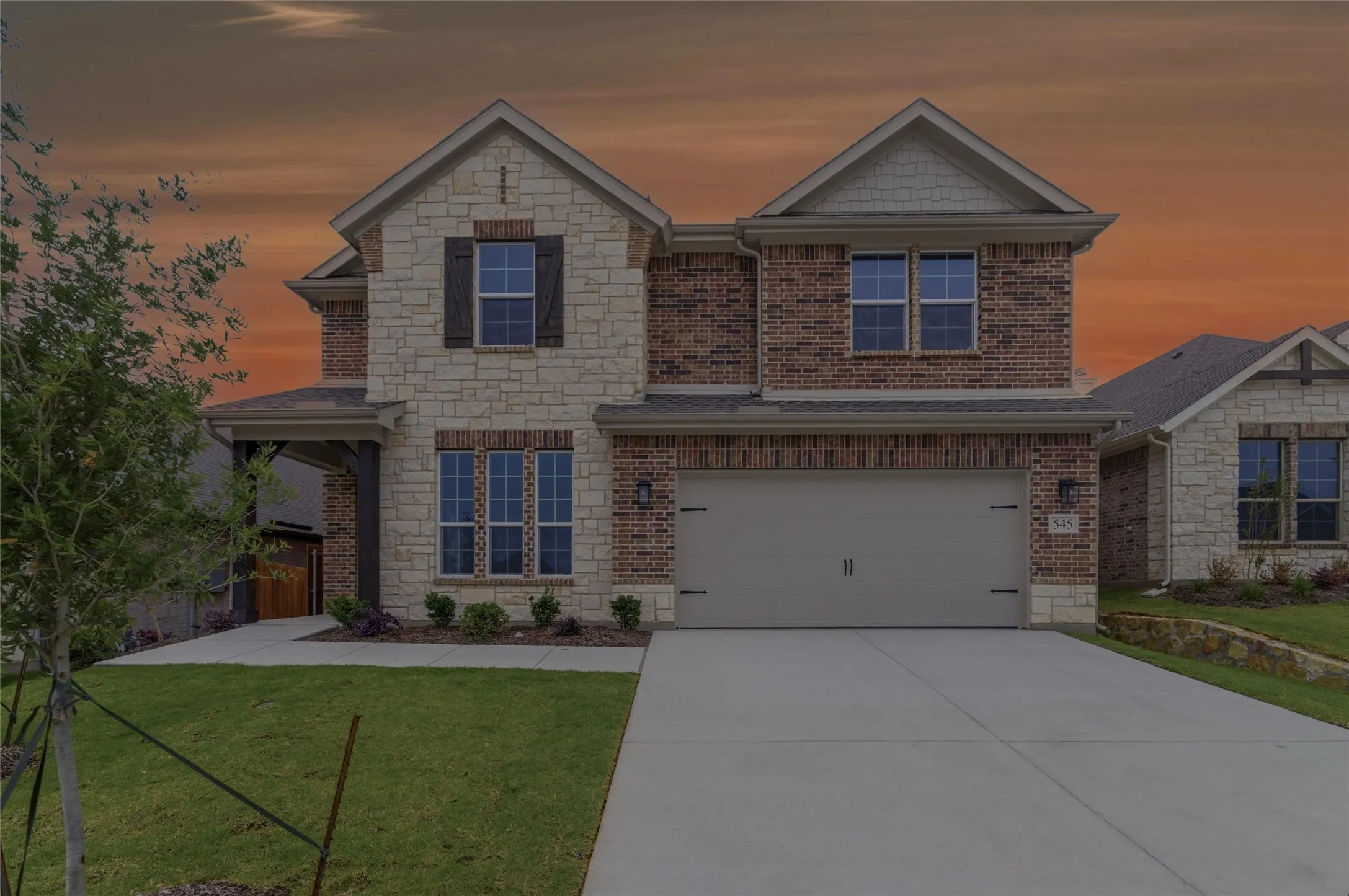 Two-story brick and stone facade residence featuring a two-car garage, covered entry, manicured lawn, and concrete driveway