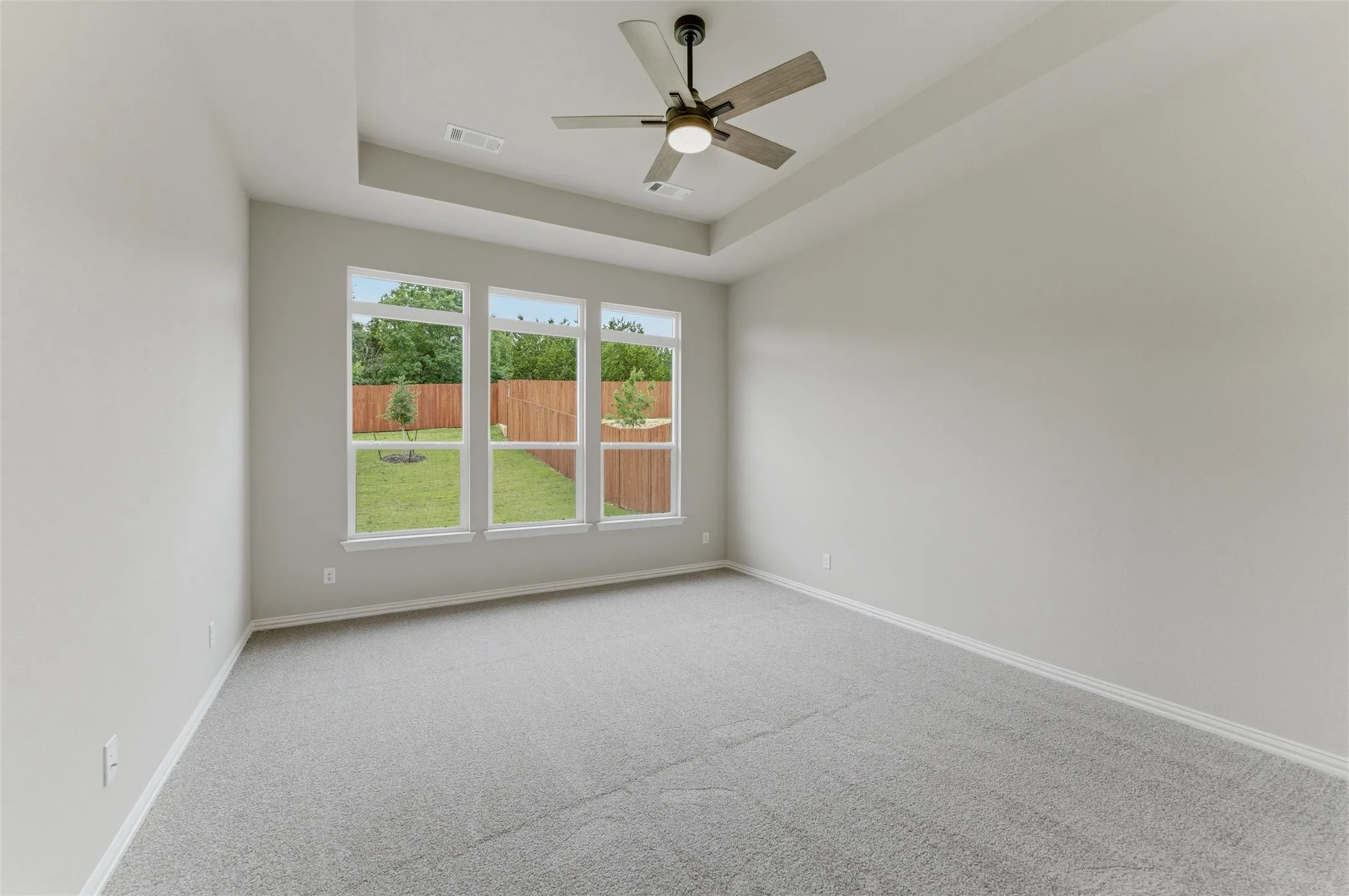 Room featuring a tray ceiling with a ceiling fan, light gray wall paint, and gray carpet