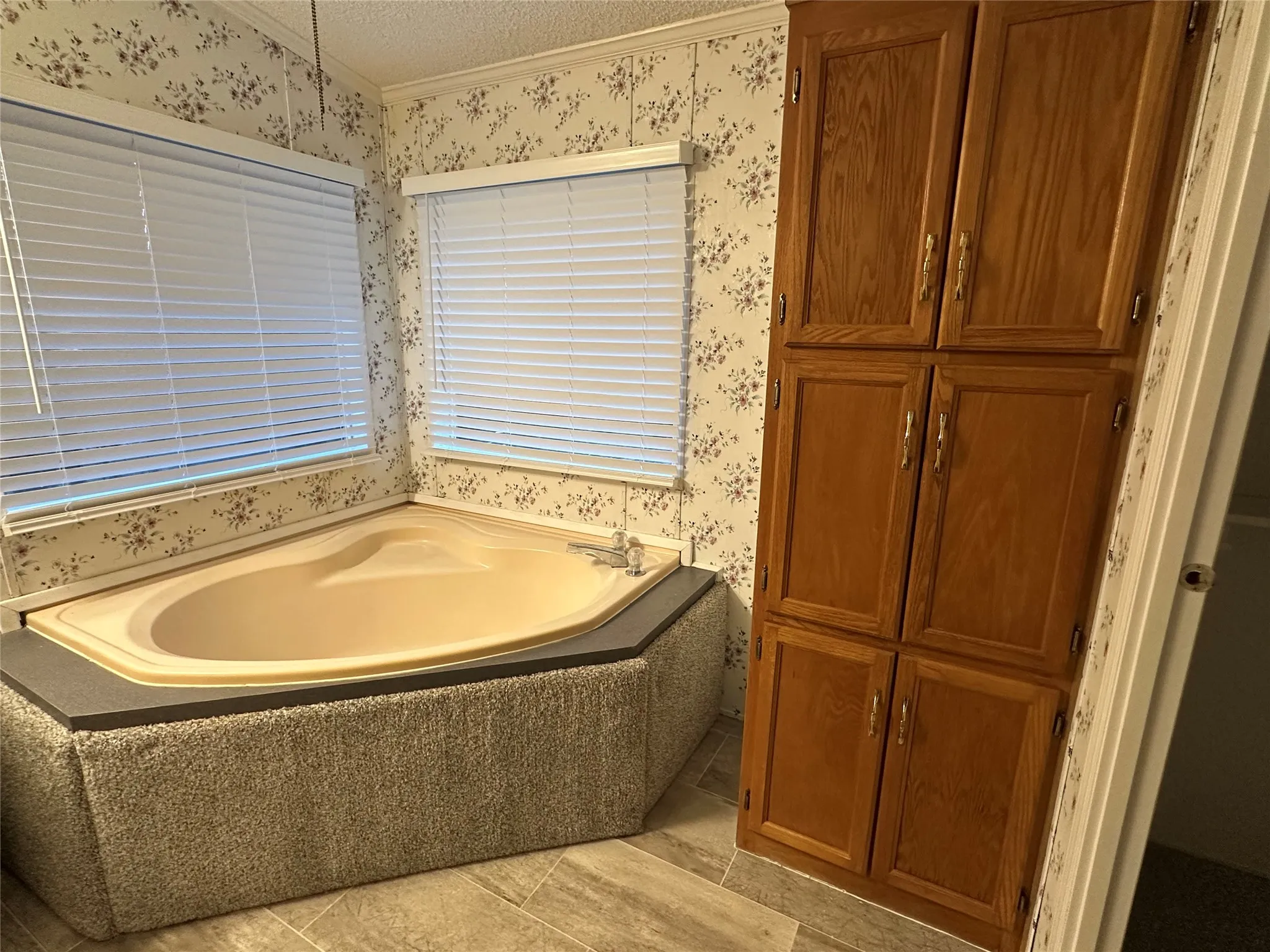 Garden tub in MBTH featuring floor to ceiling wooden linen closet.